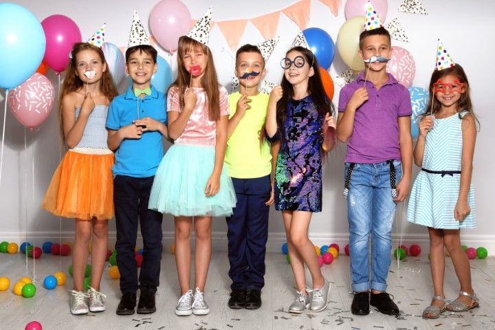 Children in party hats standing with balloons and confetti at a colorful birthday party