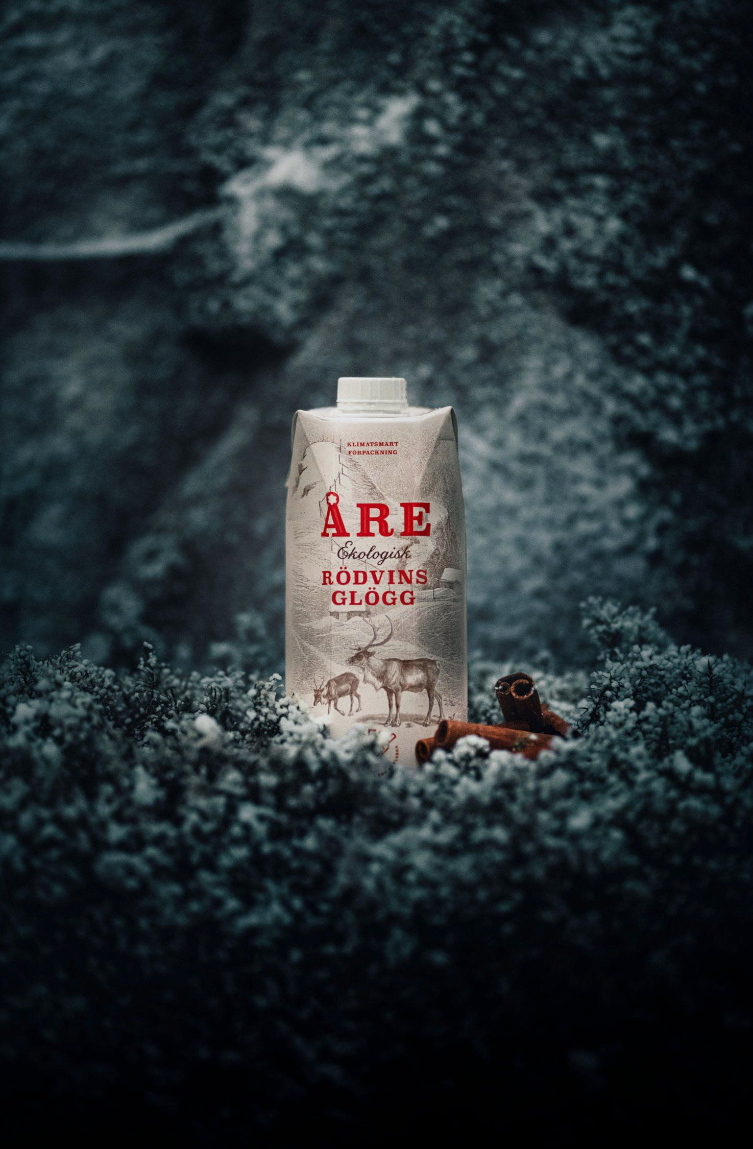 Carton of Åre Eldvarm Glögg, with text and a reindeer illustration, amid snow and cinnamon sticks.