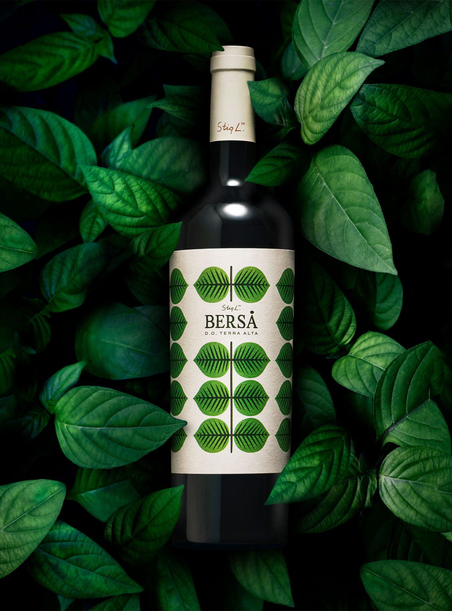 Wine bottle with green label and leaf design, surrounded by green leaves.
