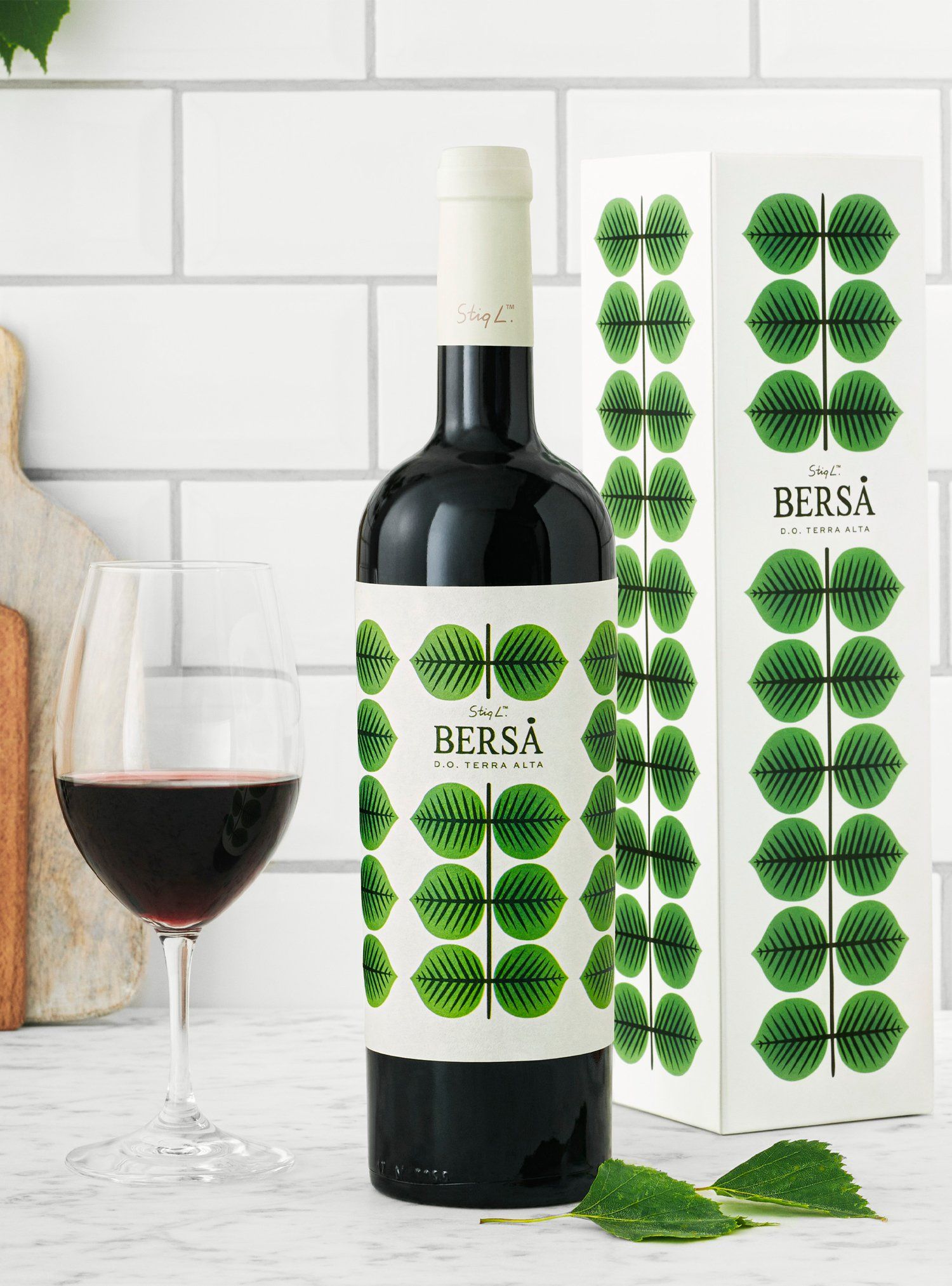 Bottle of red wine, glass, and packaging with green leaf pattern on white background.