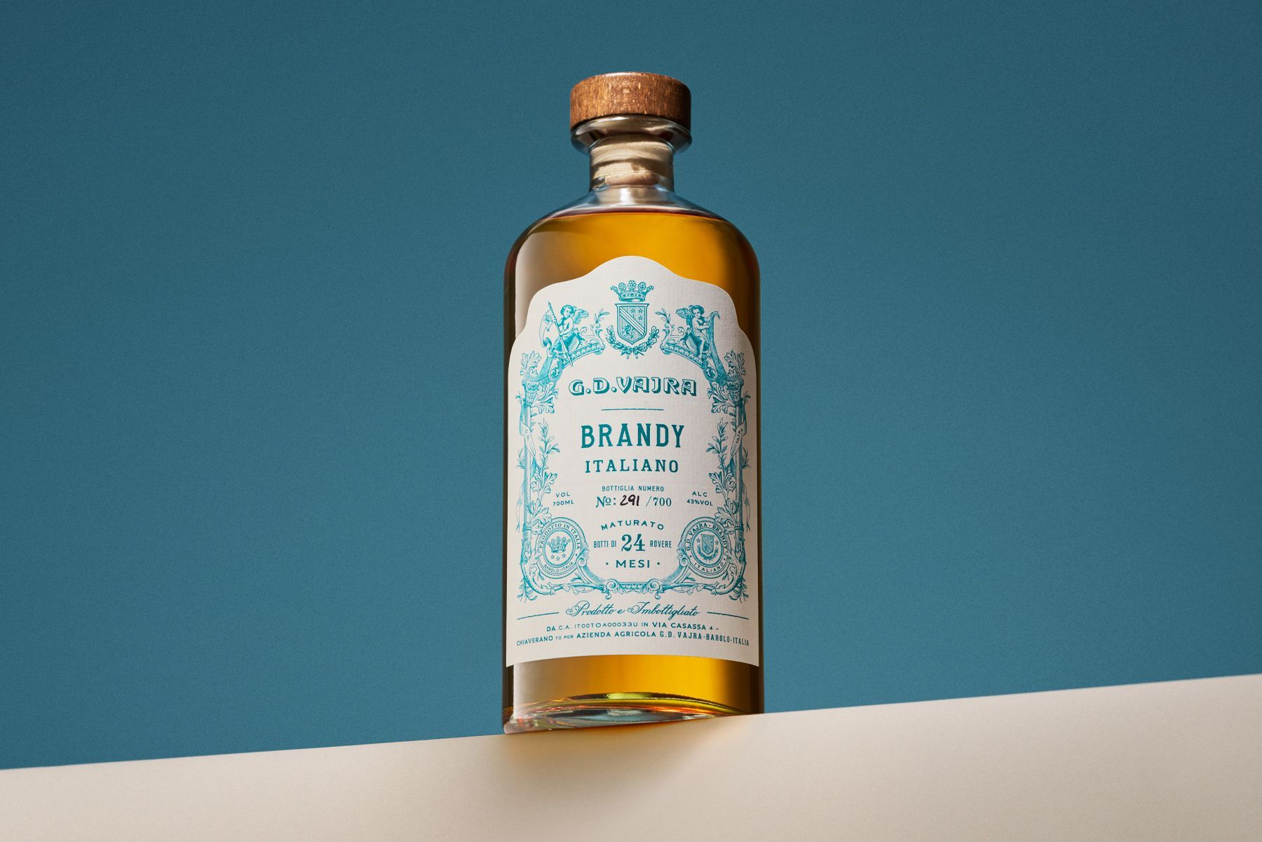 Brandy bottle from GD Vajra on a white surface against a blue backdrop; label in teal and gold.