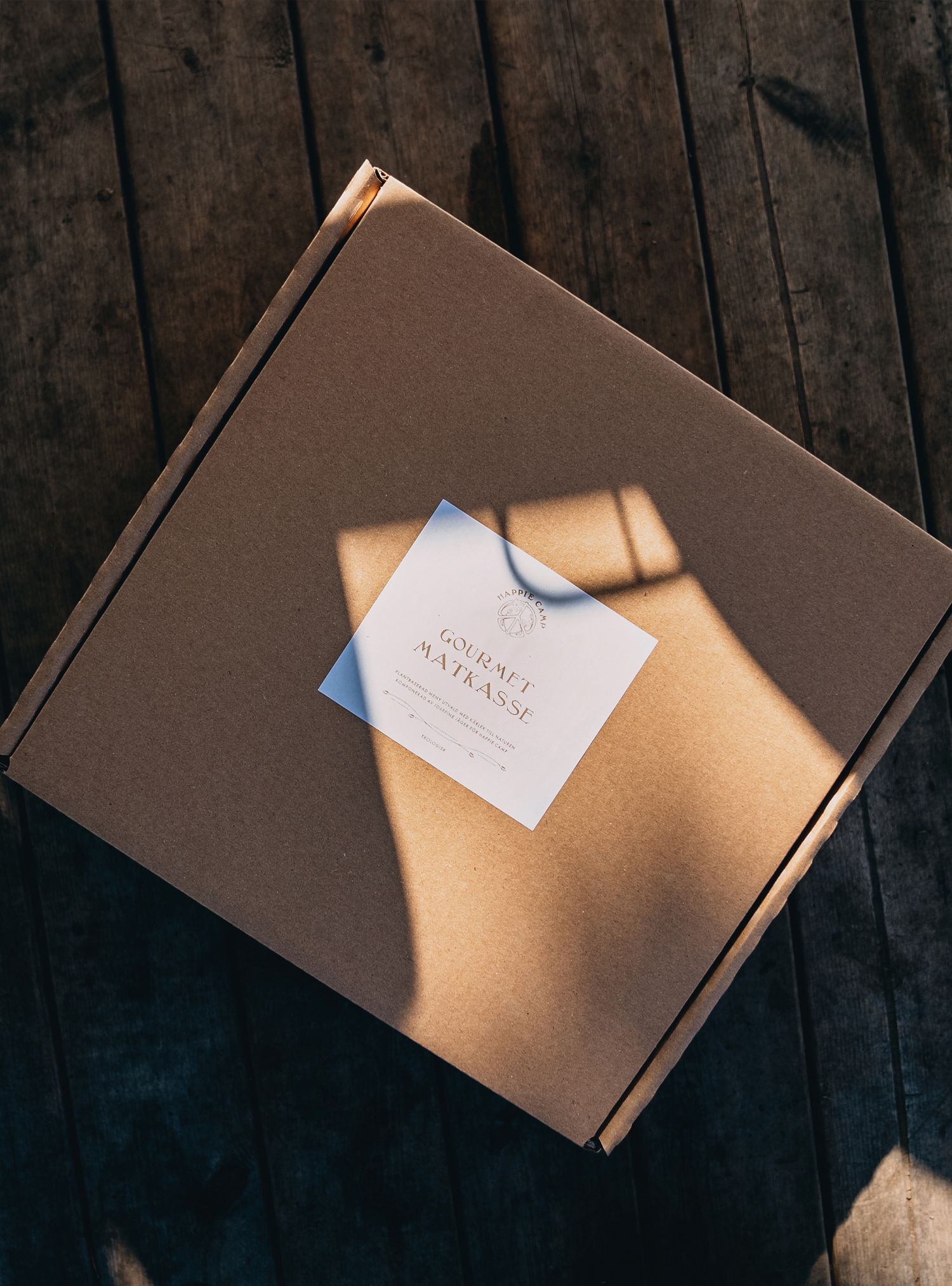 Cardboard box with a white label on a wooden surface, lit by sunlight.