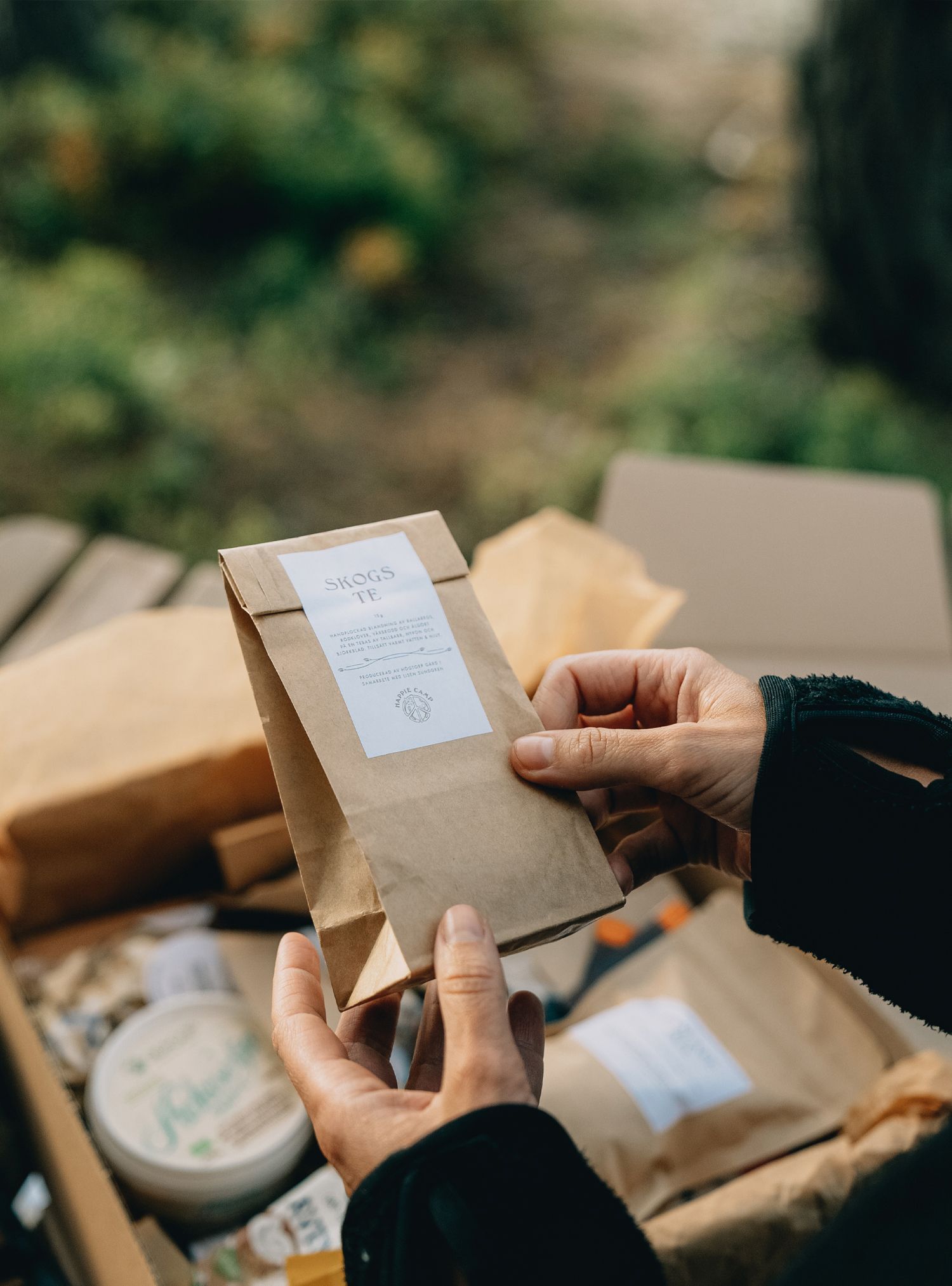 Person holding a brown paper bag with a label, part of a gift box, outdoors.