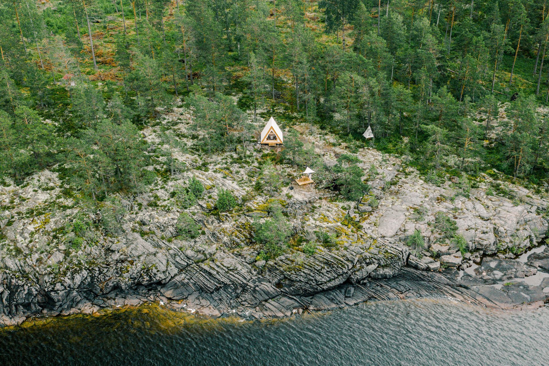Small white structure atop a rocky, tree-covered cliff overlooking dark water.