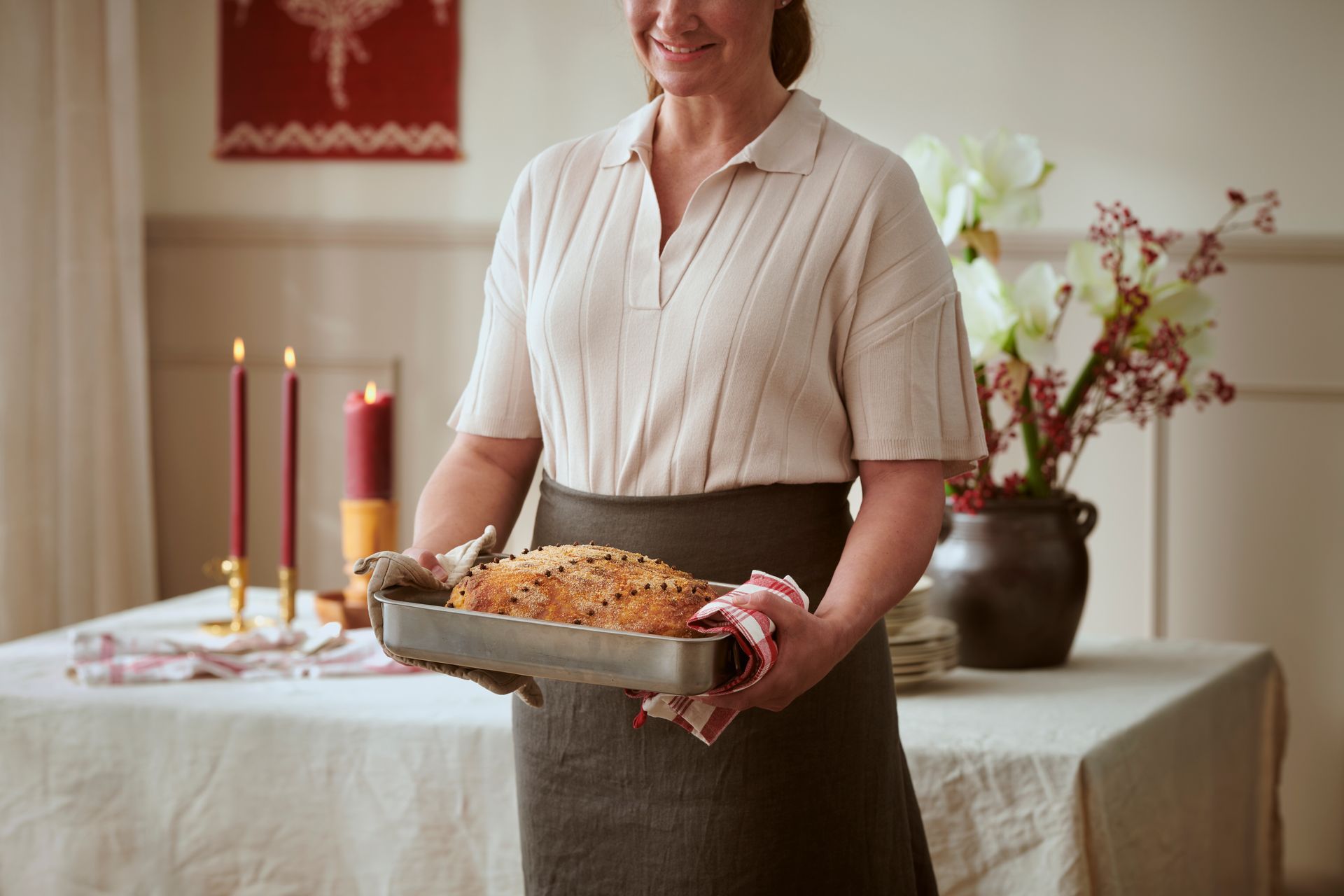 Woman holding a baking pan with baked goods, near a decorated table with candles and flowers.