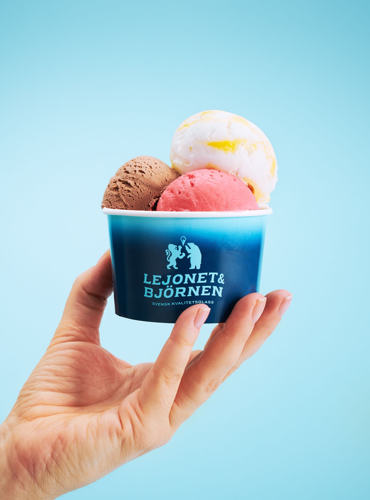 Hand holding a blue cup with three scoops of ice cream against a light blue background.