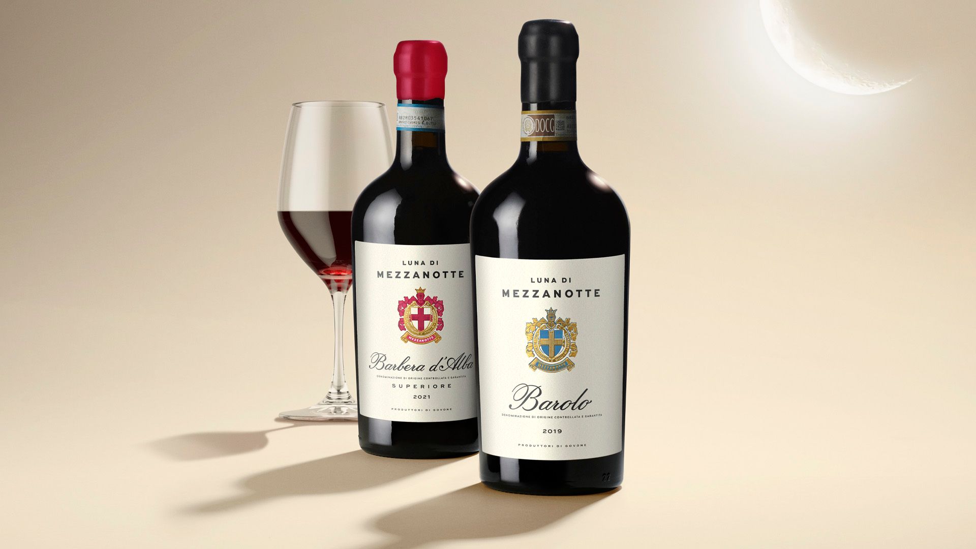 Two wine bottles with red and white labels, a glass of red wine, on a light background.