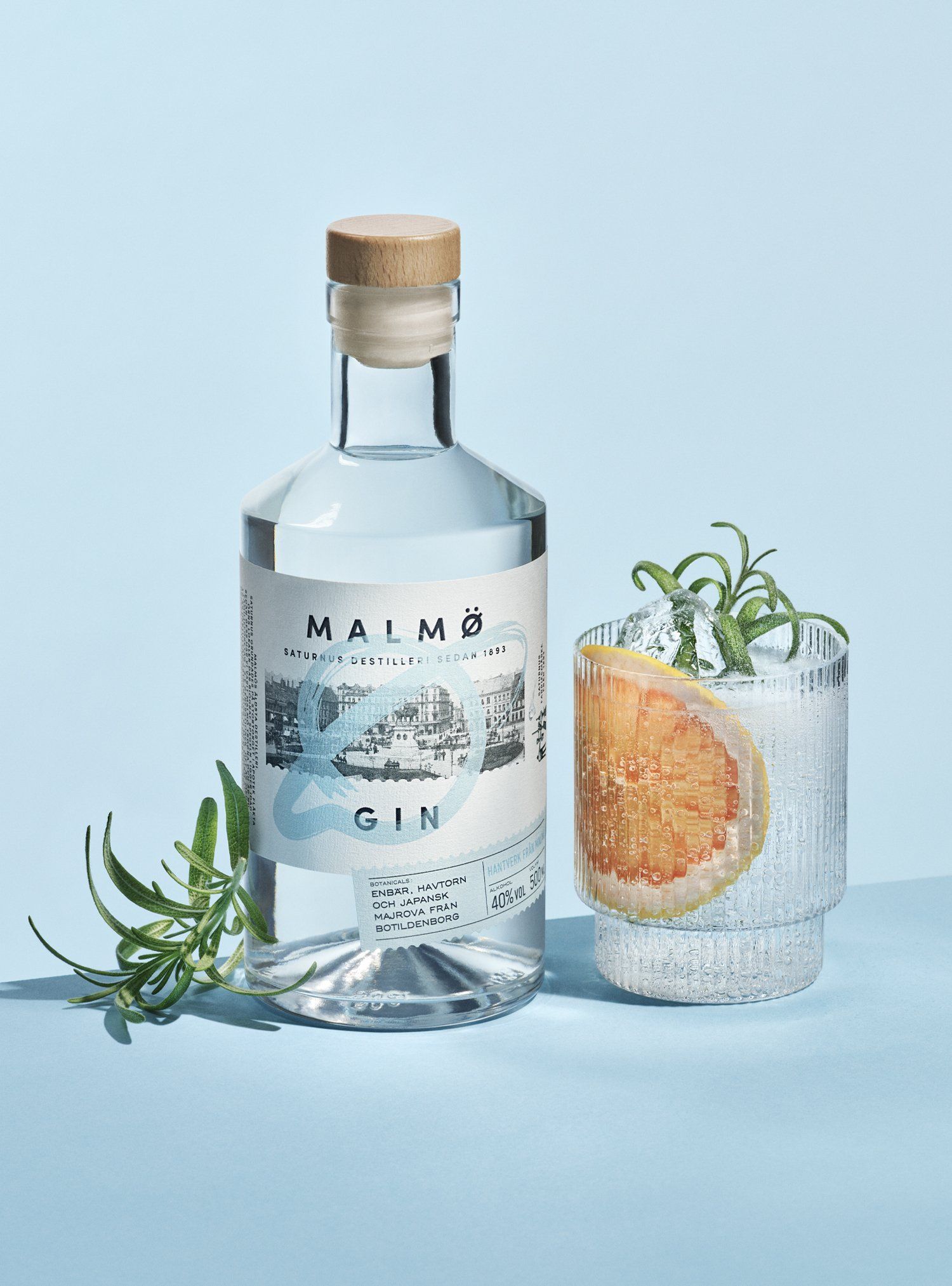 Bottle of Malmö gin with a glass of gin and tonic garnished with grapefruit and rosemary.