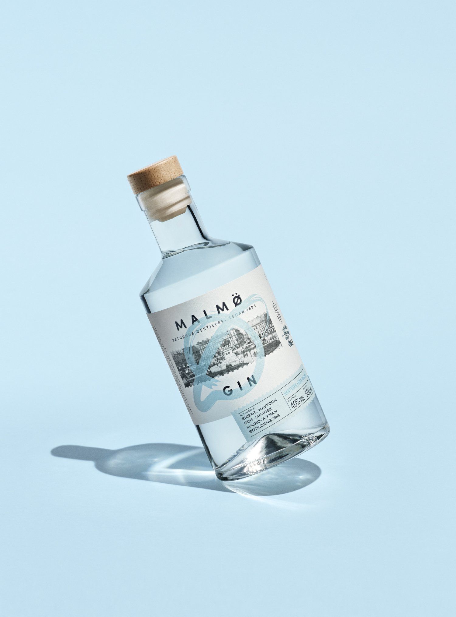 Gin bottle, leaning, with a white and blue label, on a light blue background.