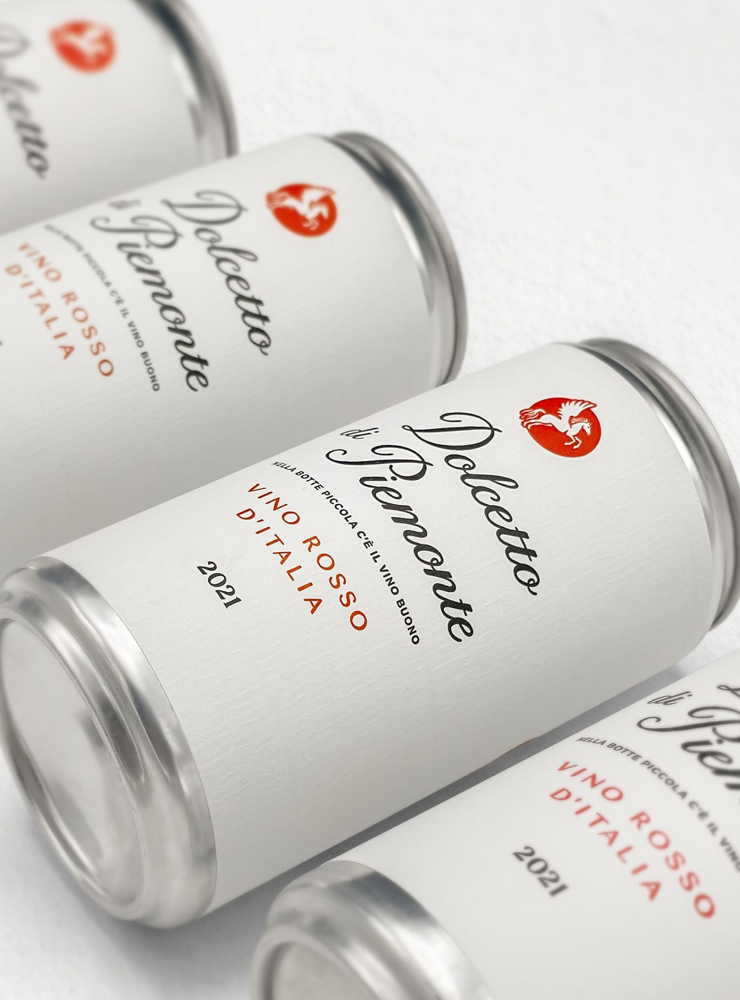 Four cans of Dolcetto Piemonte wine. White label with black text and a red logo.