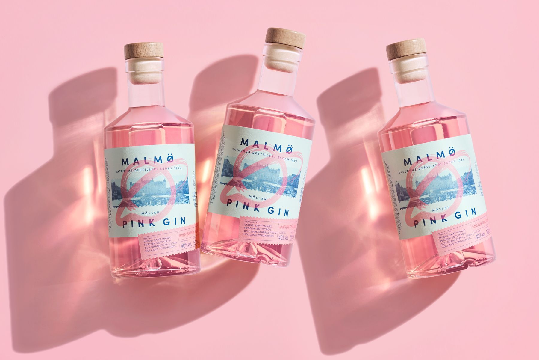 Three pink gin bottles on a pink background, bottles tilted with labels reading 