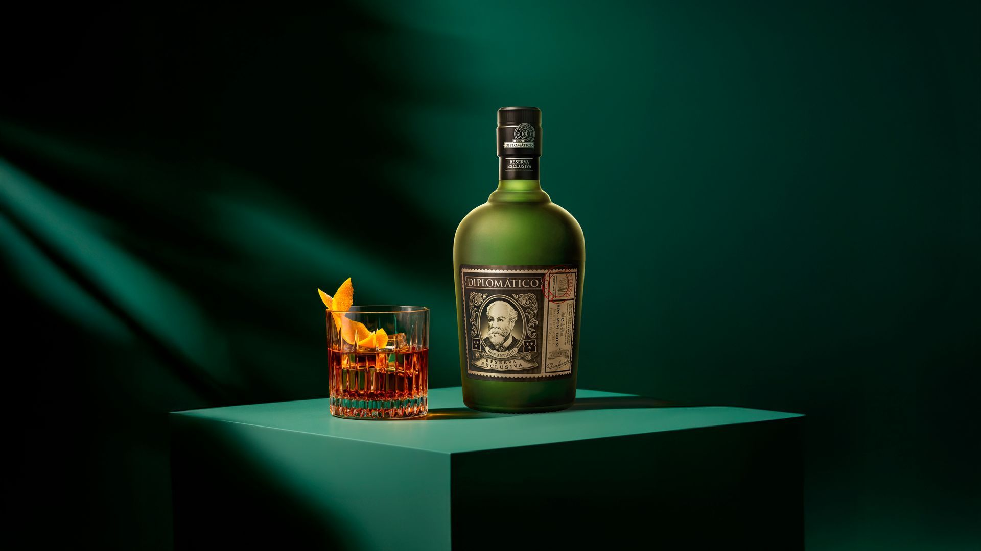 Bottle of green rum next to a cocktail on a green cube with a dark green background.
