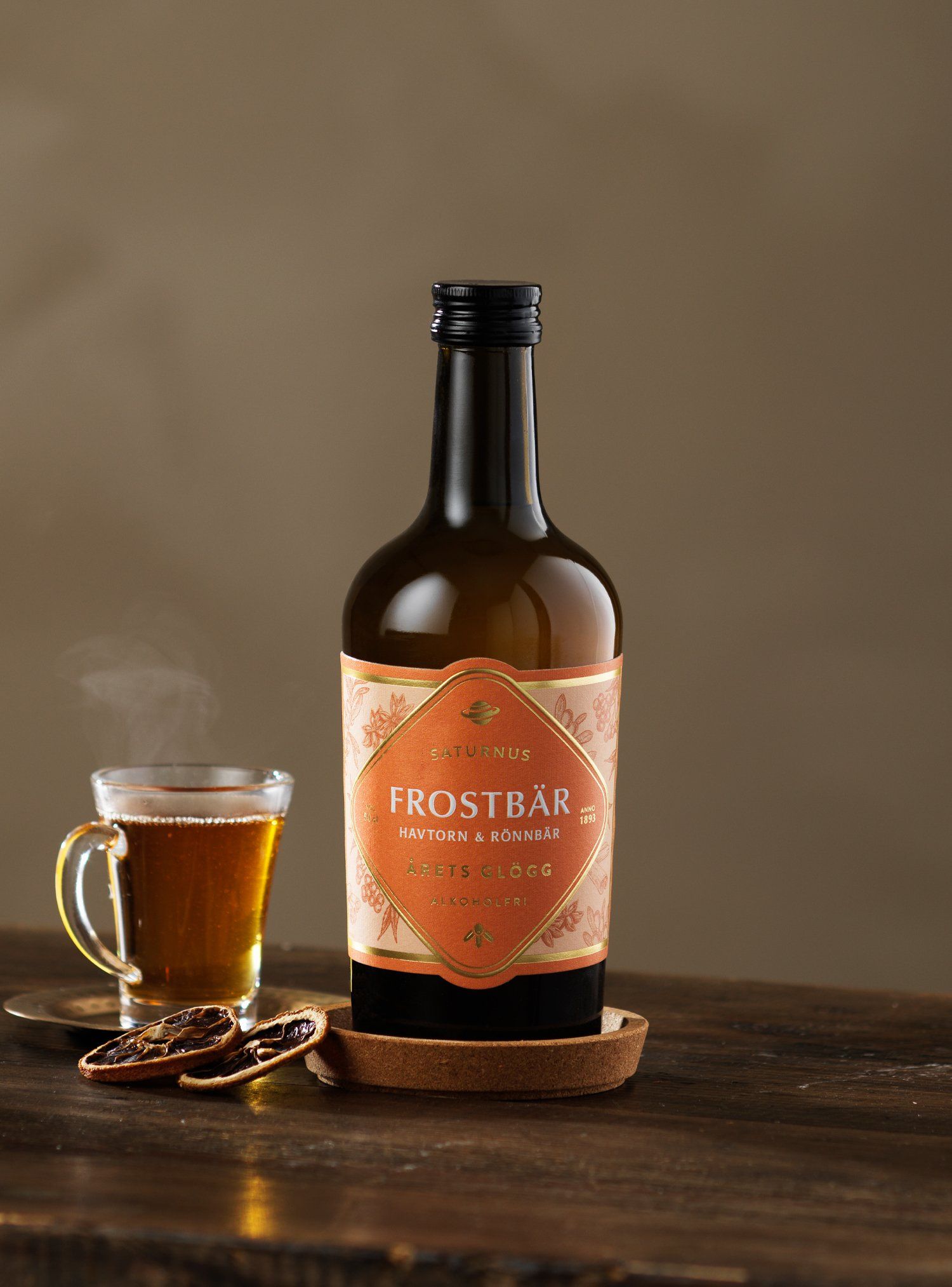 Bottle of Frostbär liqueur next to a steaming cup and dried orange slices on a wooden surface.