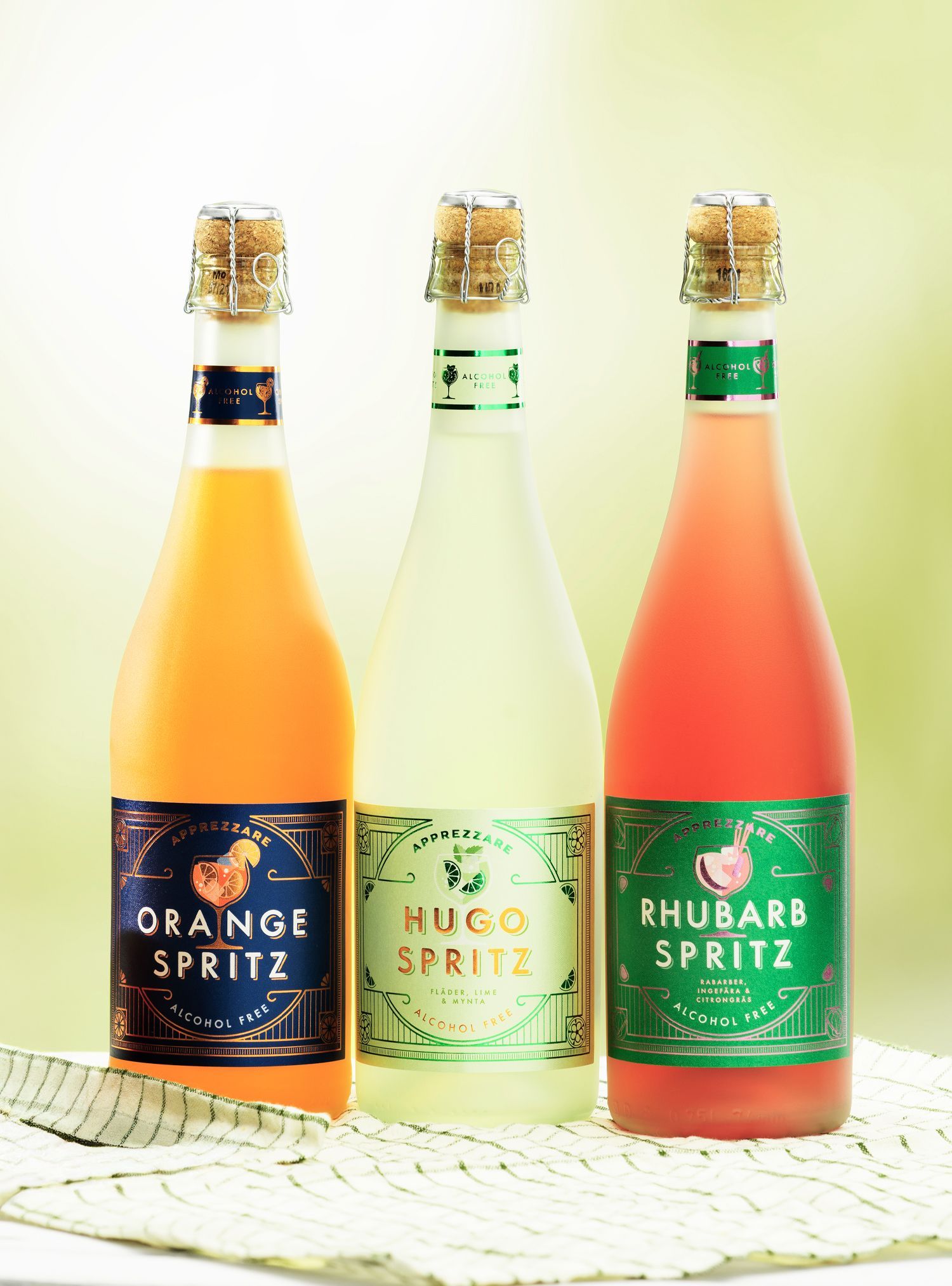 Three bottles of spritz drinks from Saturnus: orange, hugo, and rhubarb, on a table.