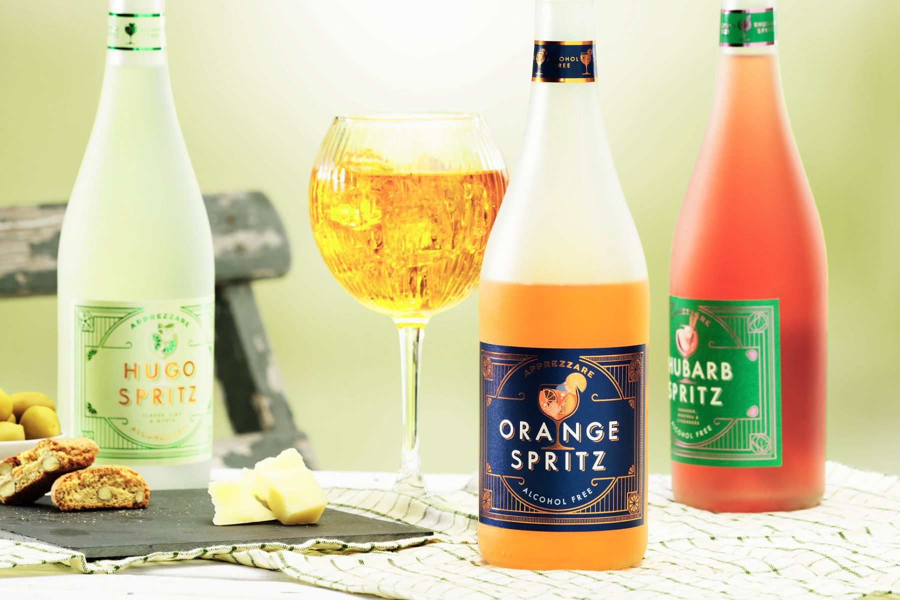 Three colorful spritz bottles, from Saturnus, a wine glass, and snacks on a table.