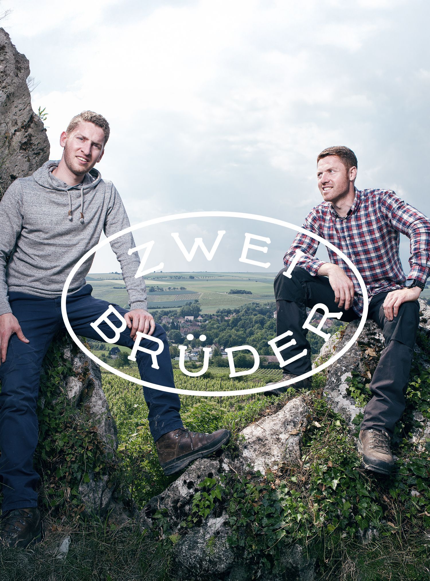 Two men seated on a rock with a valley backdrop. Text