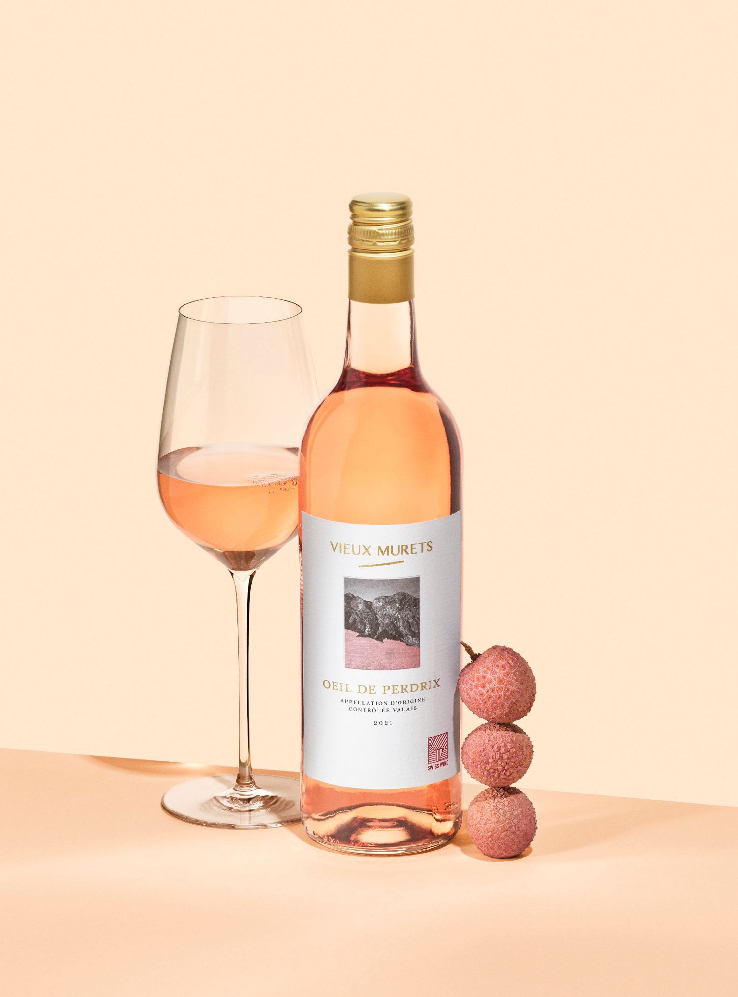 Bottle and glass of pink wine with lychee fruit on peach background.