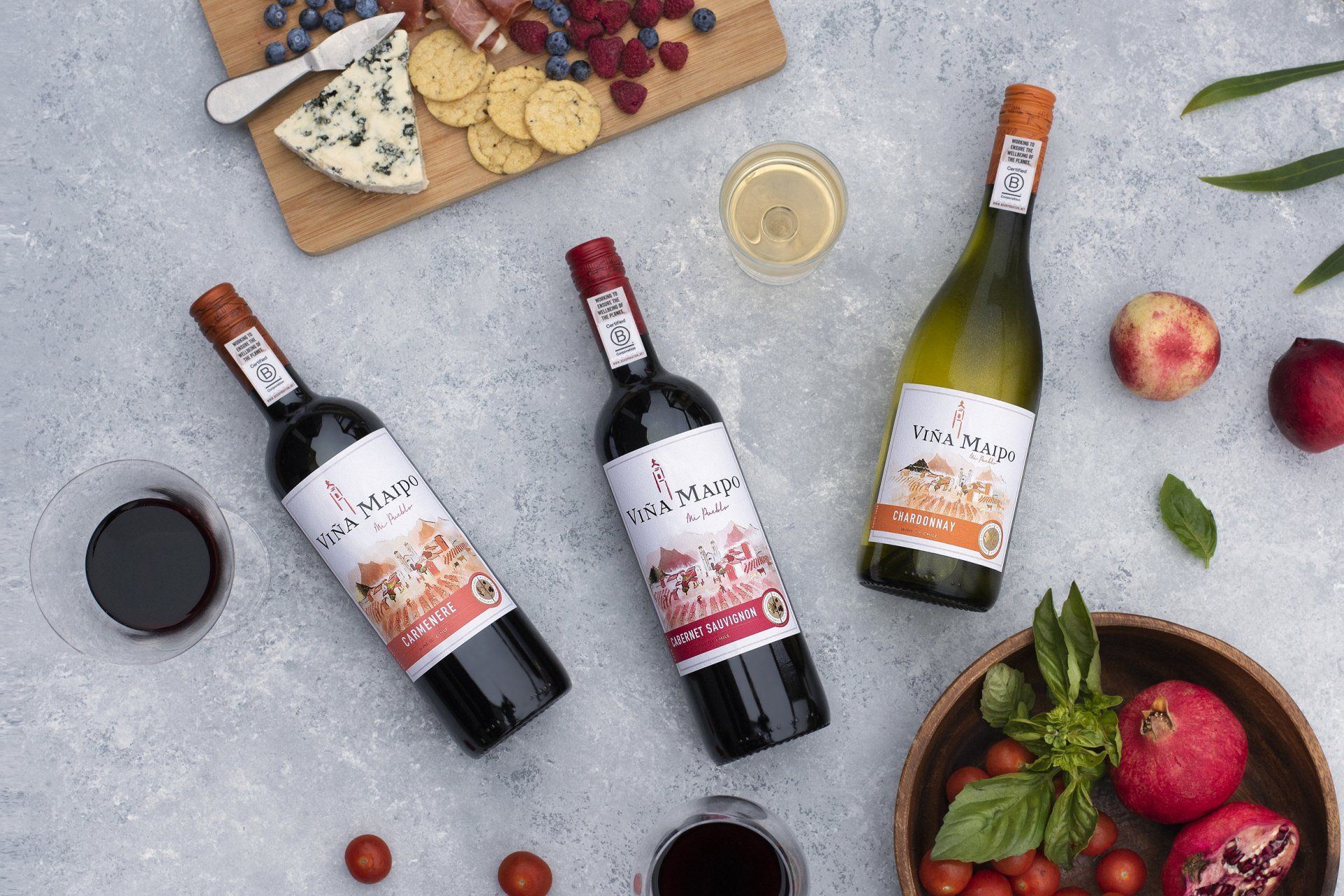 Wine bottles and snacks: red wine, white wine, cheese board with fruit, tomatoes, pomegranate.