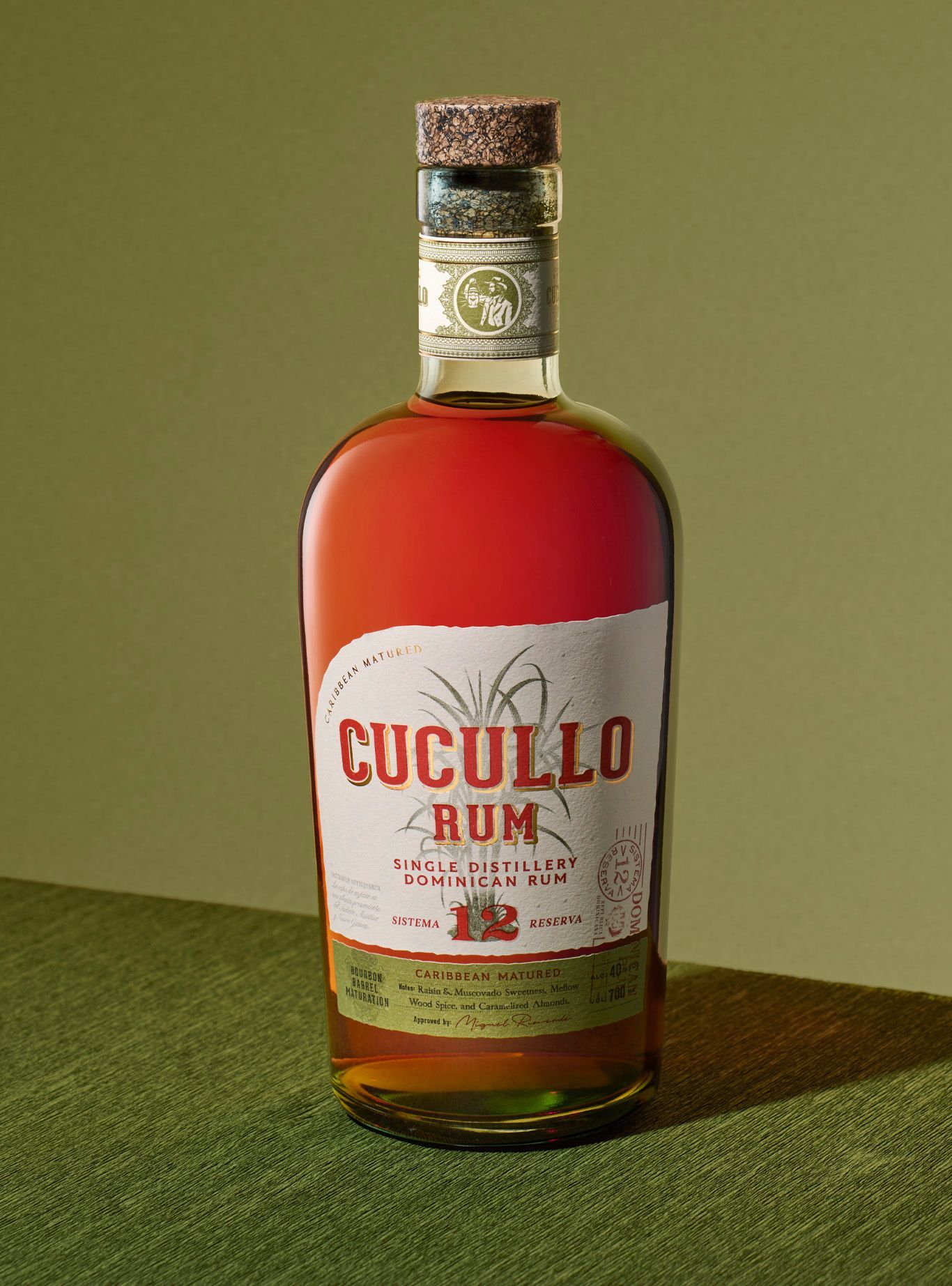 Bottle of Cucullo Rum with red and white label, cork top, and green background.