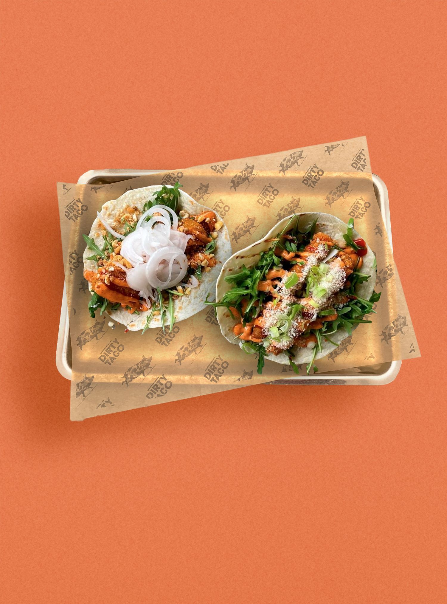 Two tacos on a metal tray with patterned paper on an orange background.