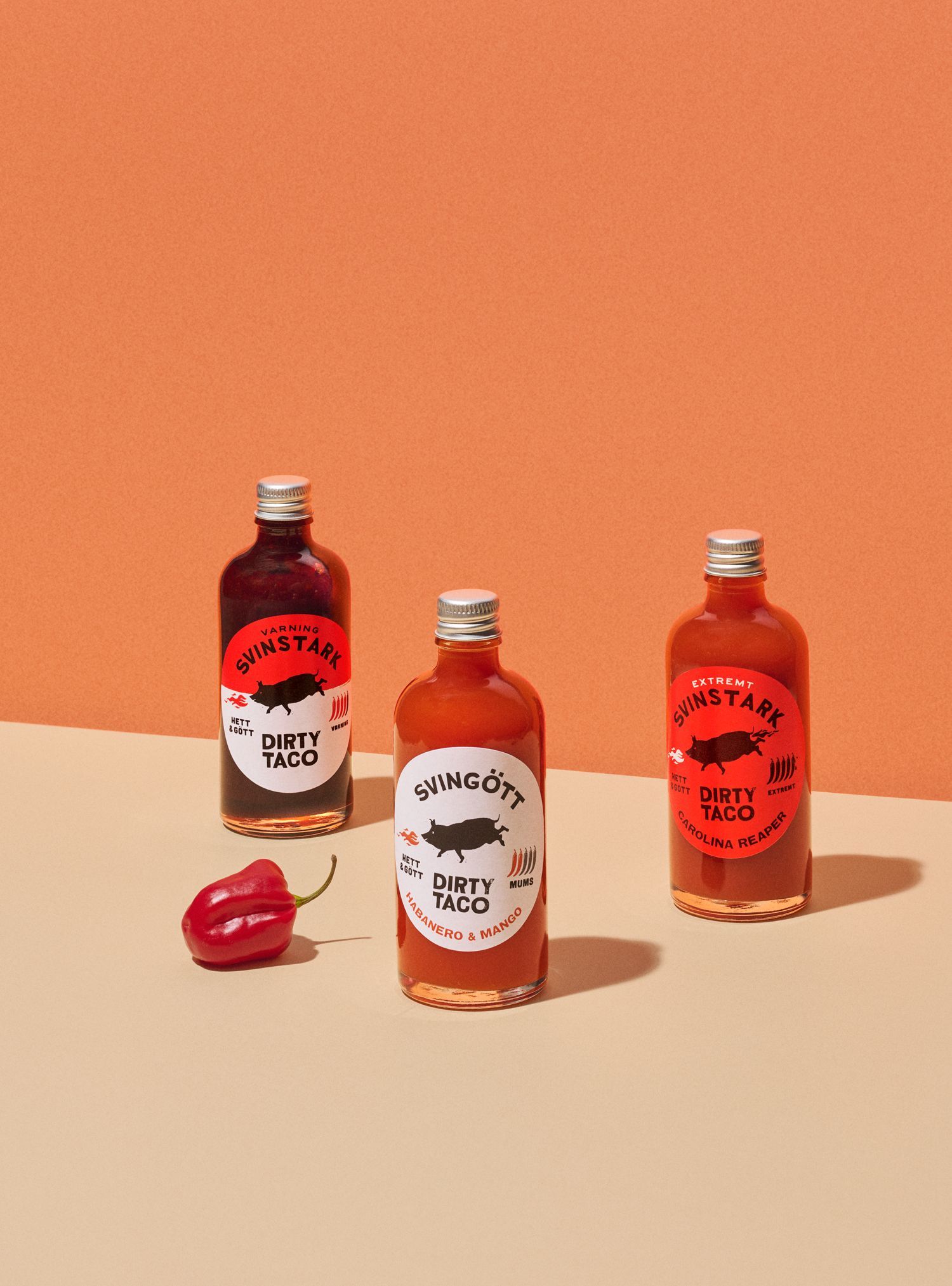 Three bottles of hot sauce with a pepper on a peach-colored background.