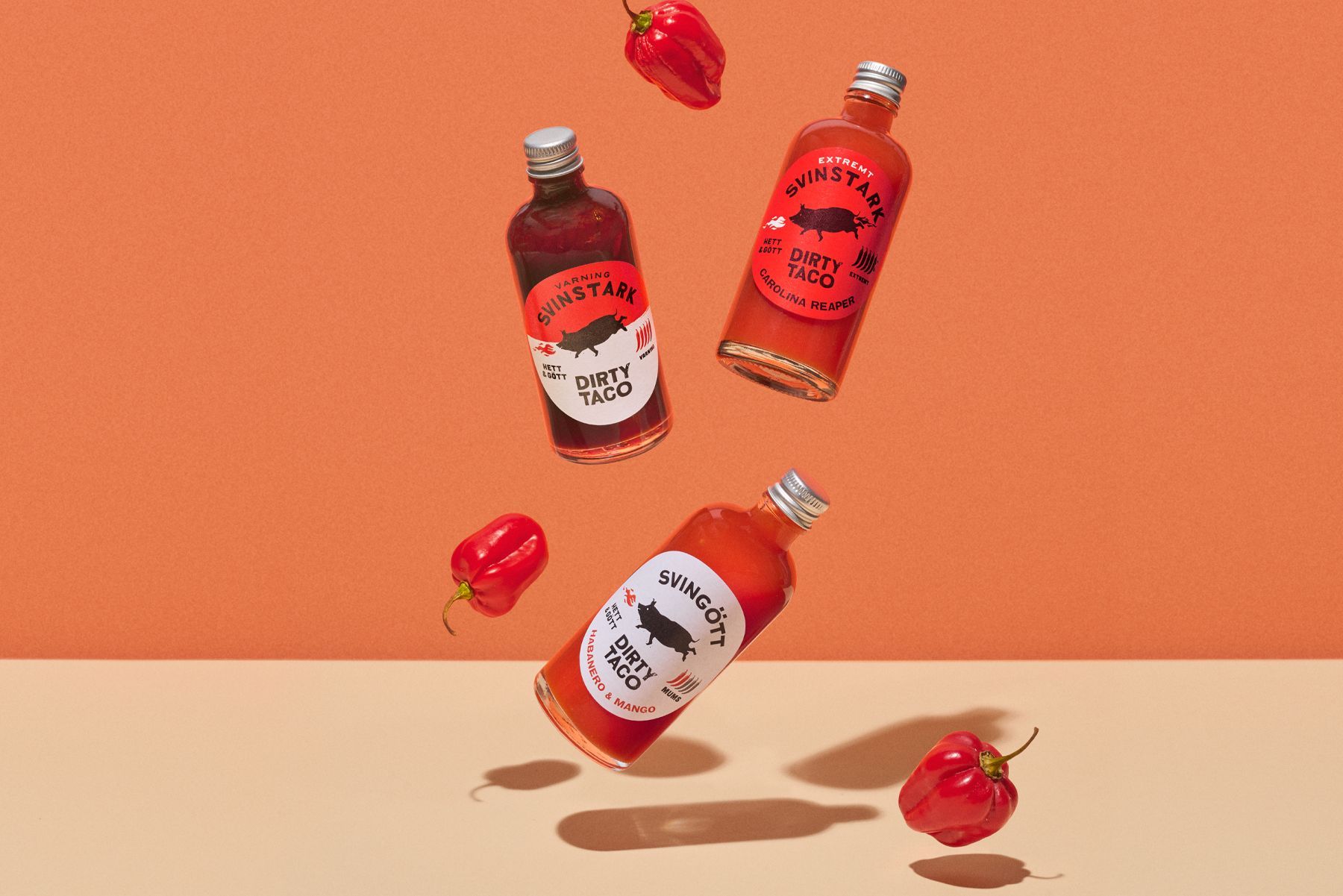 Three bottles of hot sauce, from Dirty Taco, and red peppers levitating against an orange backdrop.