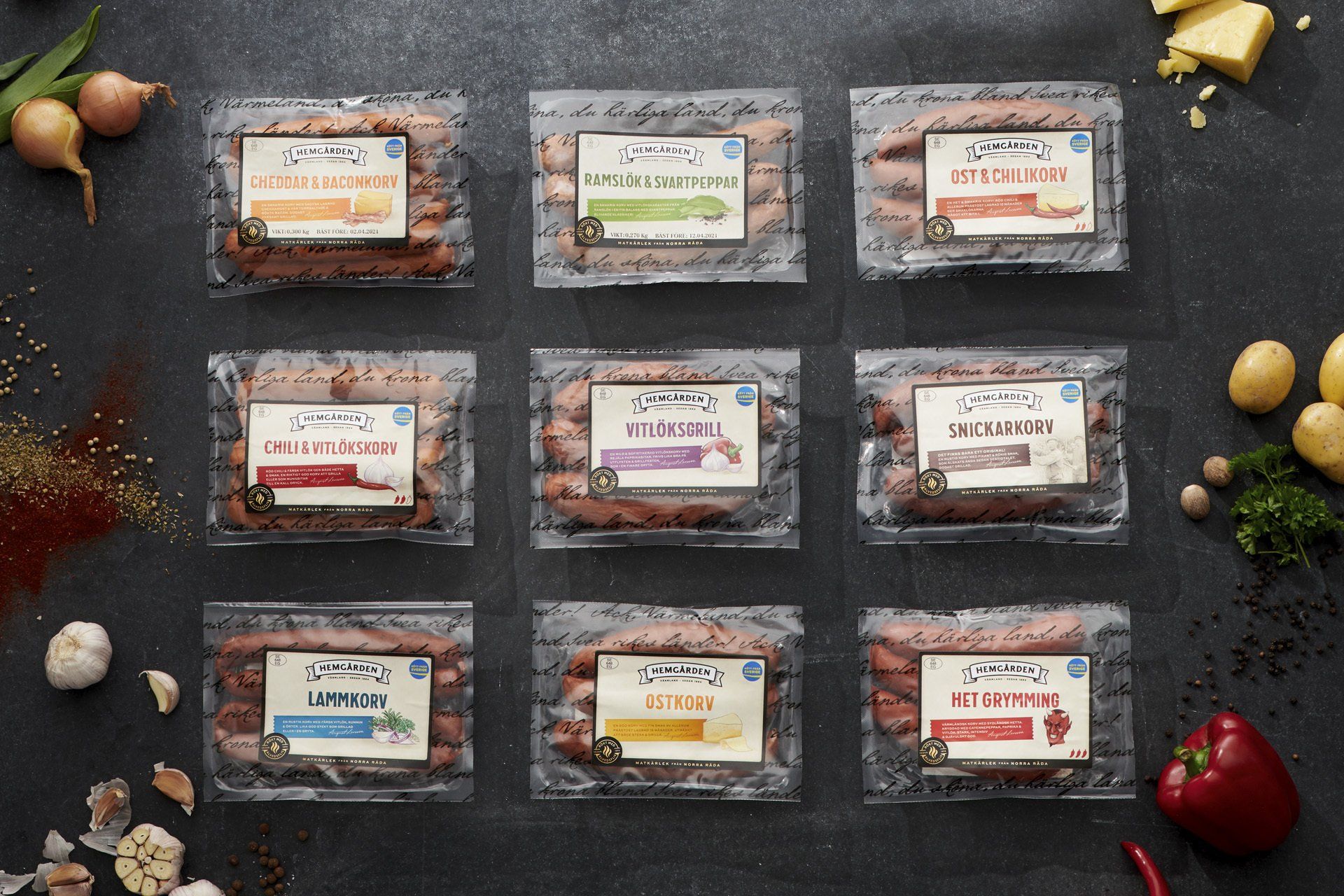Nine packages of sausages on a dark surface, surrounded by ingredients like onions, spices, and potatoes.