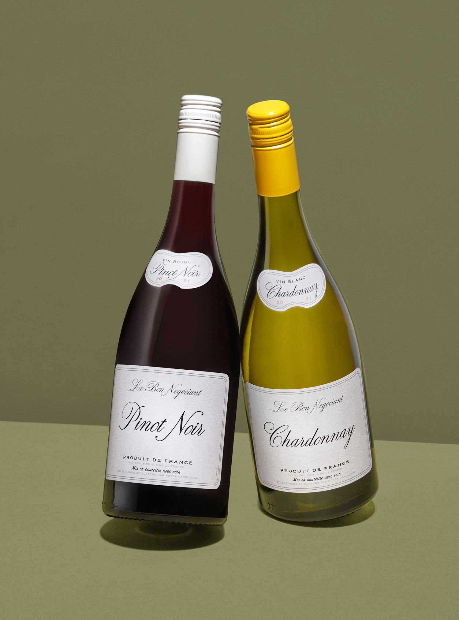 Two wine bottles: a red Pinot Noir and a yellow Chardonnay, leaning against each other on a green background.