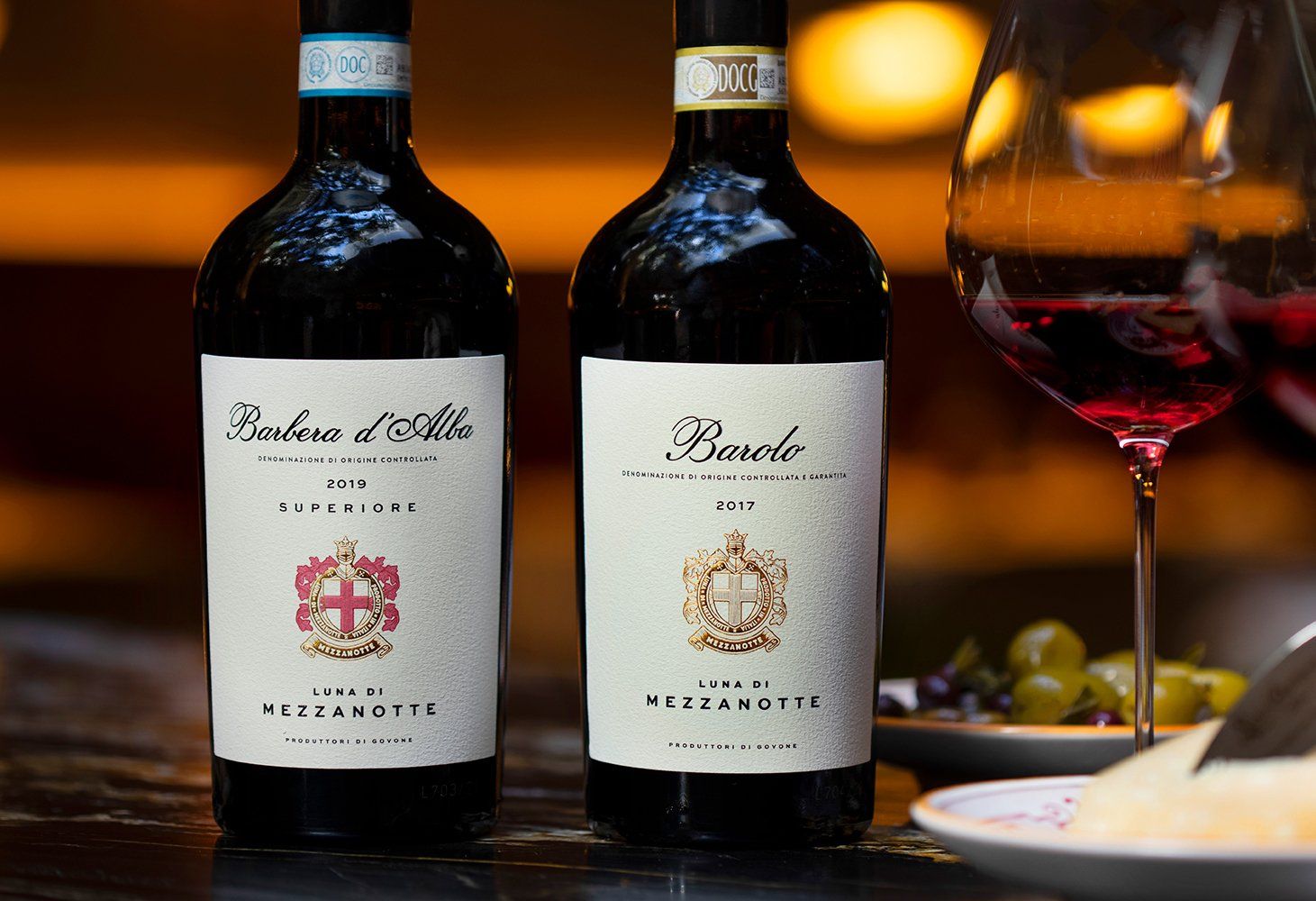 Two wine bottles, Luna di mezzanotte, near glasses of red wine and grapes.