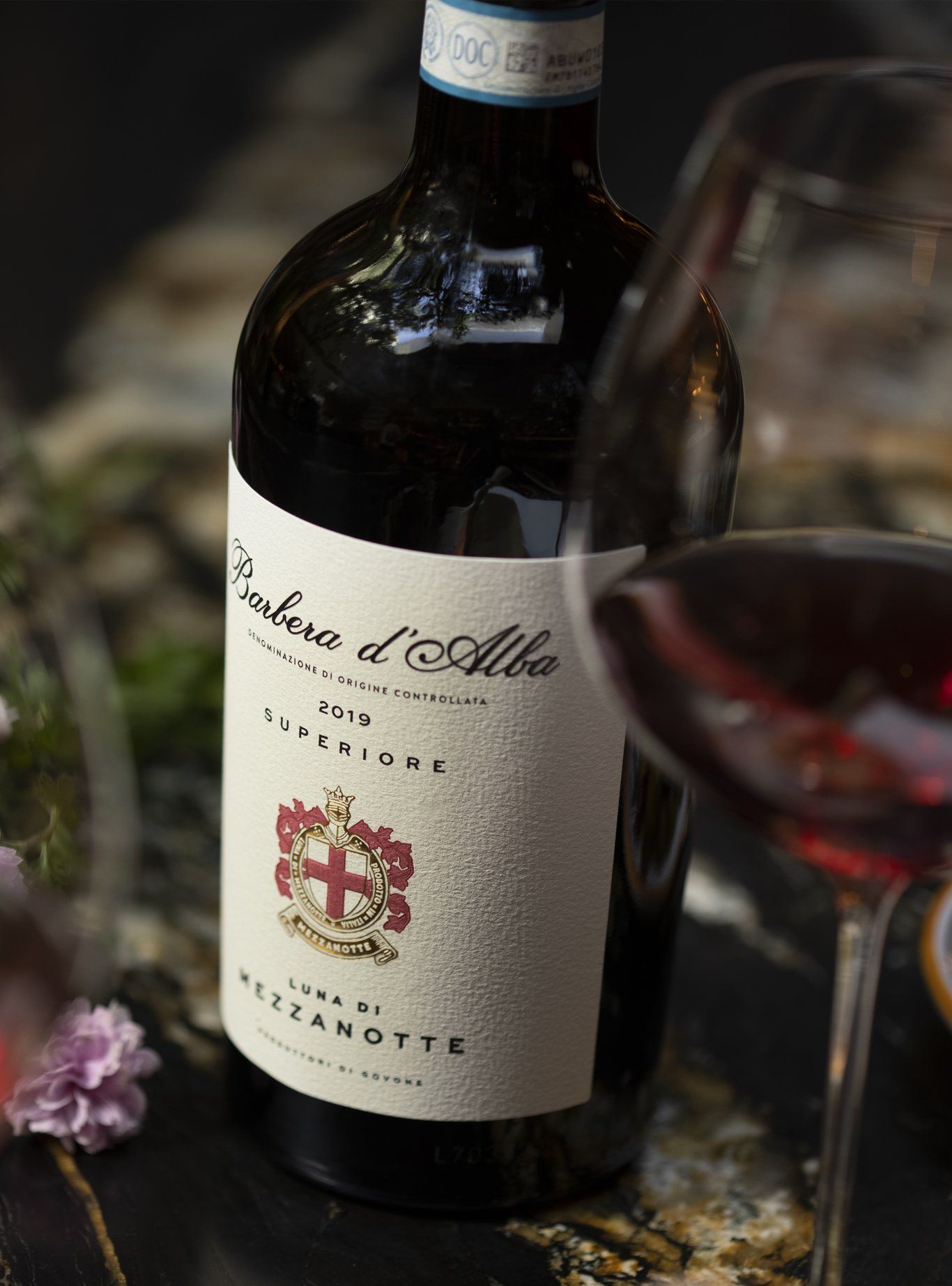 Wine bottle and glass with red wine, label details visible, on a dark surface.