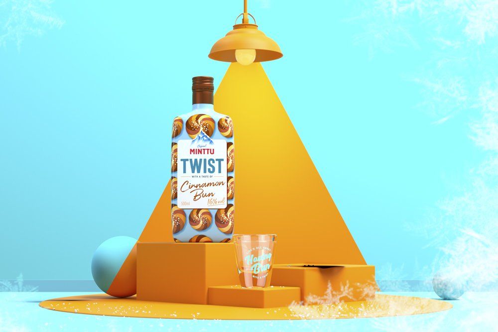 Bottle of WITT cinnamon twist liqueur on an orange stand, lit by a lamp. A shot glass sits nearby on a blue backdrop.