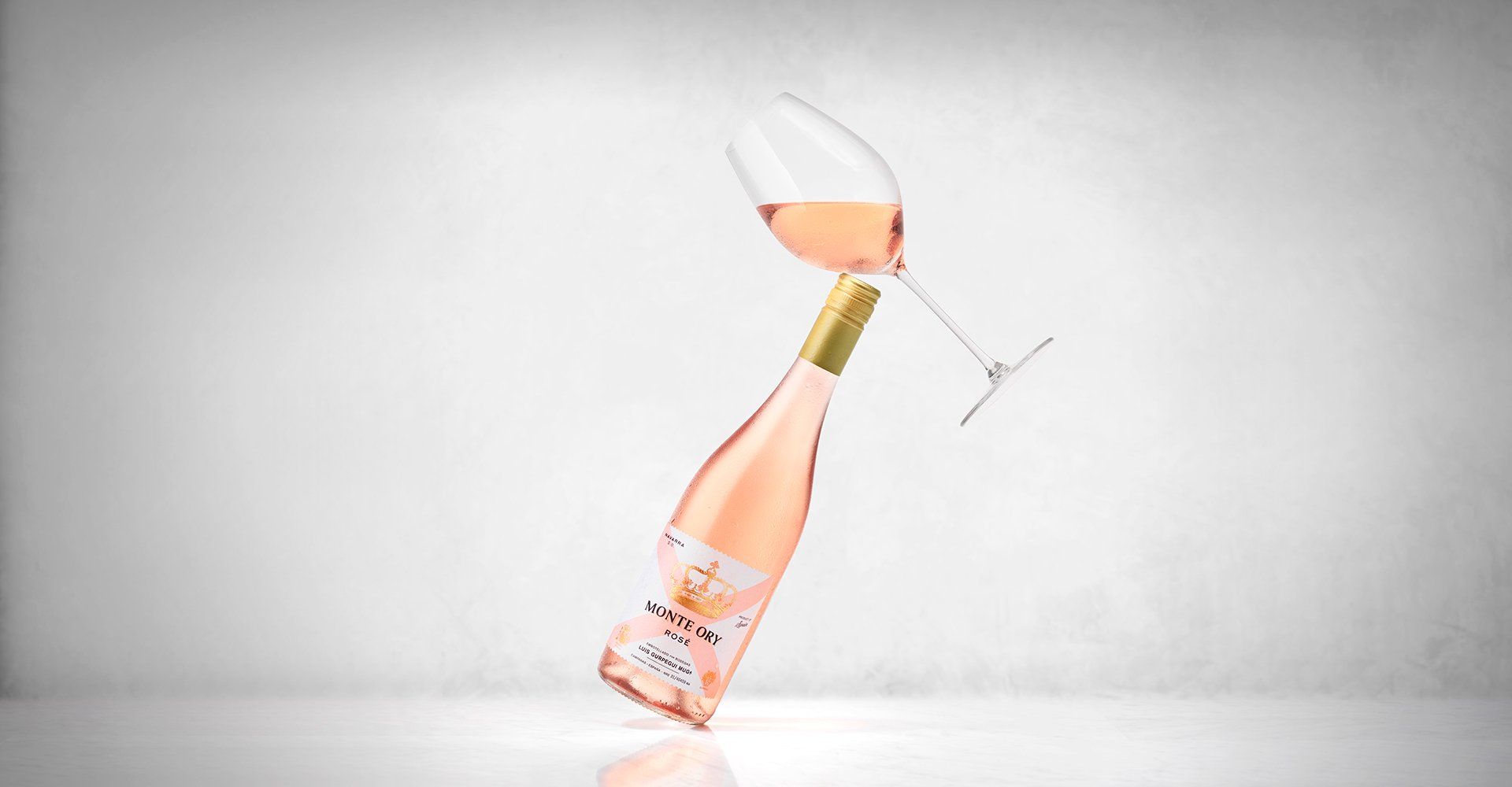 Bottle and glass of pink wine balanced upright.