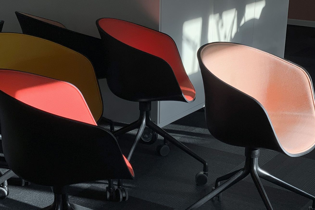 Office chairs: black base, colored interiors (yellow, red, orange, peach), arranged in a group.