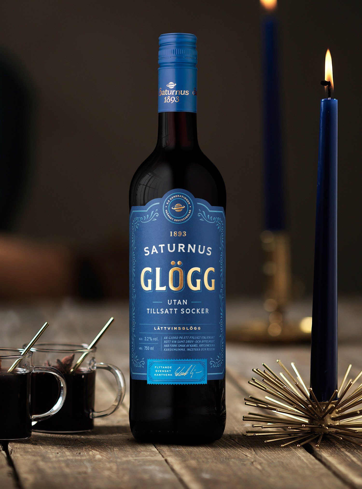 Bottle of Saturnus Glögg, two candles, and two mugs on a wooden table.