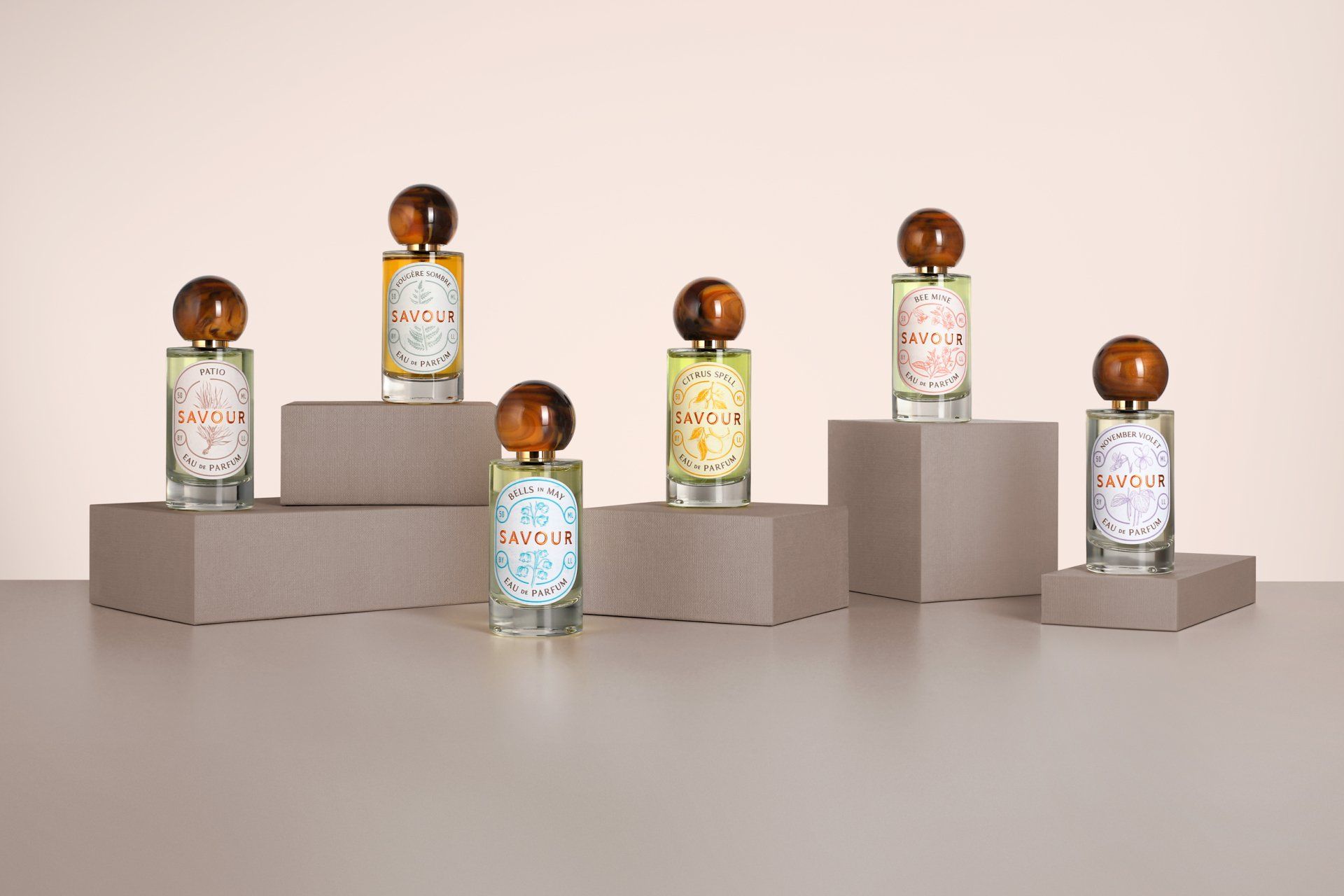 Seven perfume bottles with brown caps and labels, arranged on gray risers, against a light beige background.