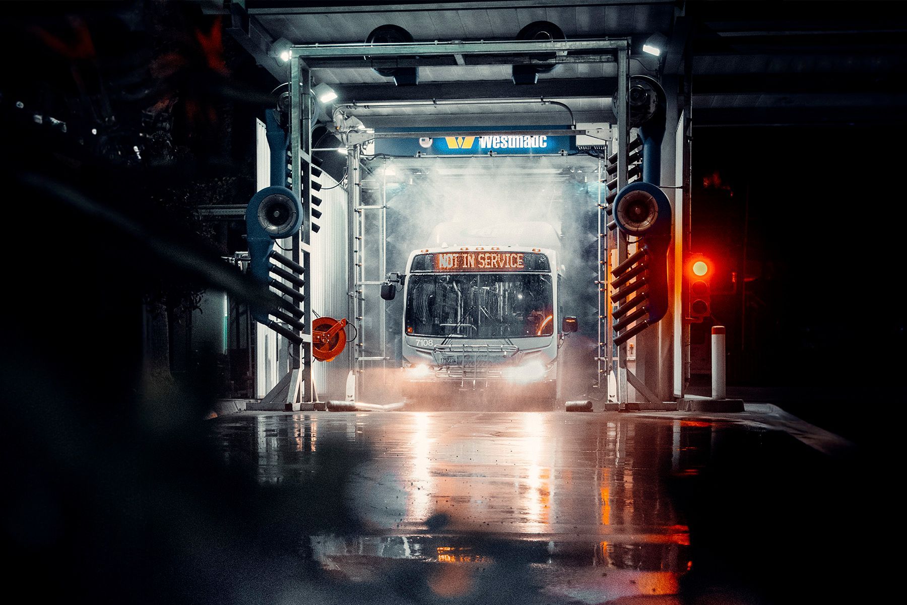 A bus inside a car wash at night; water and lights create a misty glow.