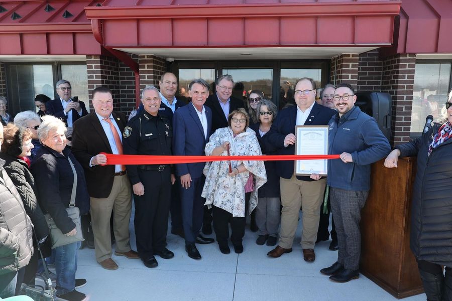 A group of people cutting a red ribbon in front of a building