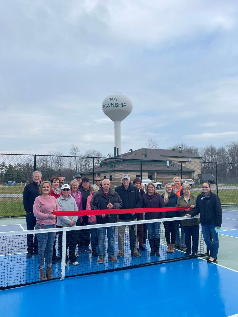 A group of people are cutting a red ribbon on a tennis court.