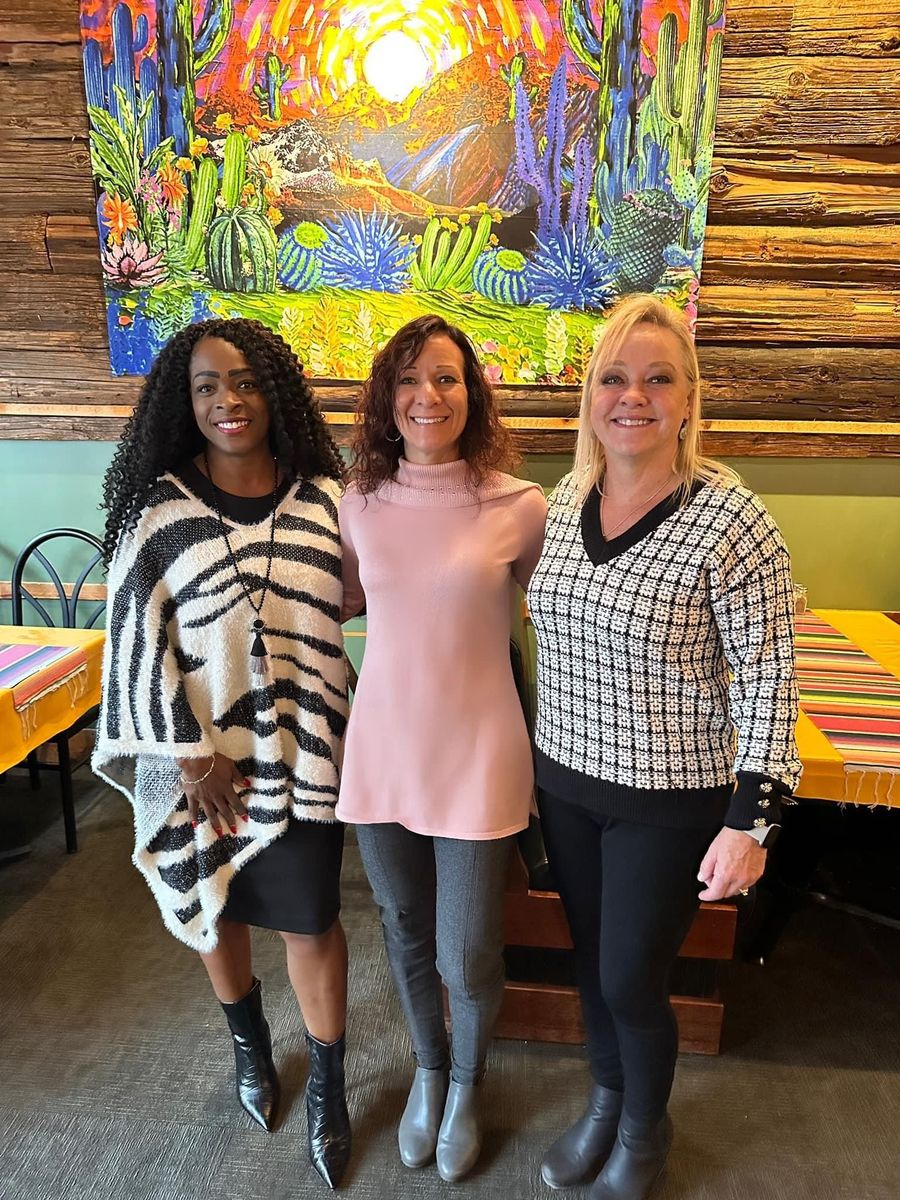 Three women are posing for a picture in front of a painting