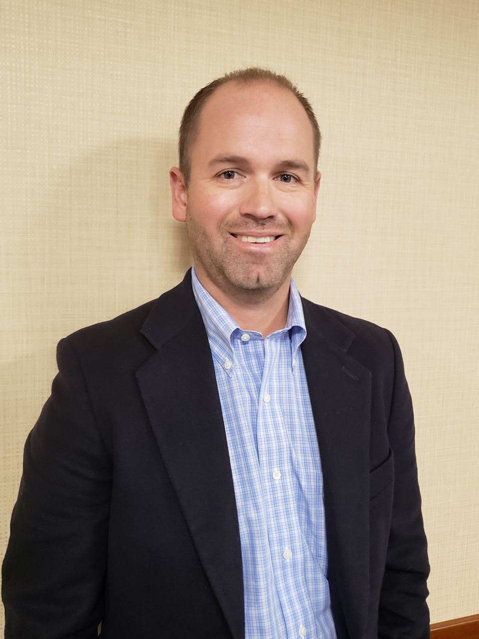 A man in a suit and blue shirt is smiling for the camera