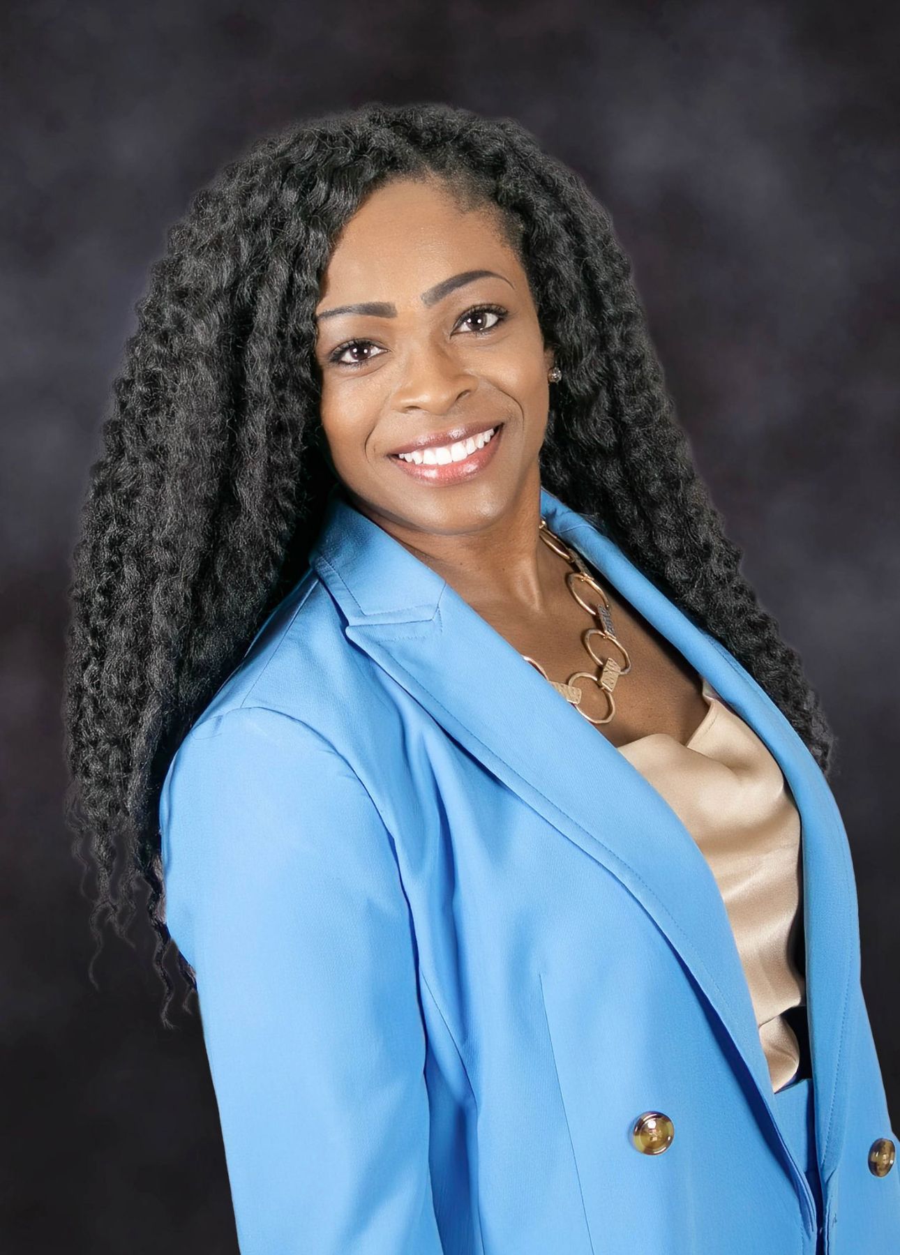 A woman with dreadlocks is wearing a blue jacket and smiling.
