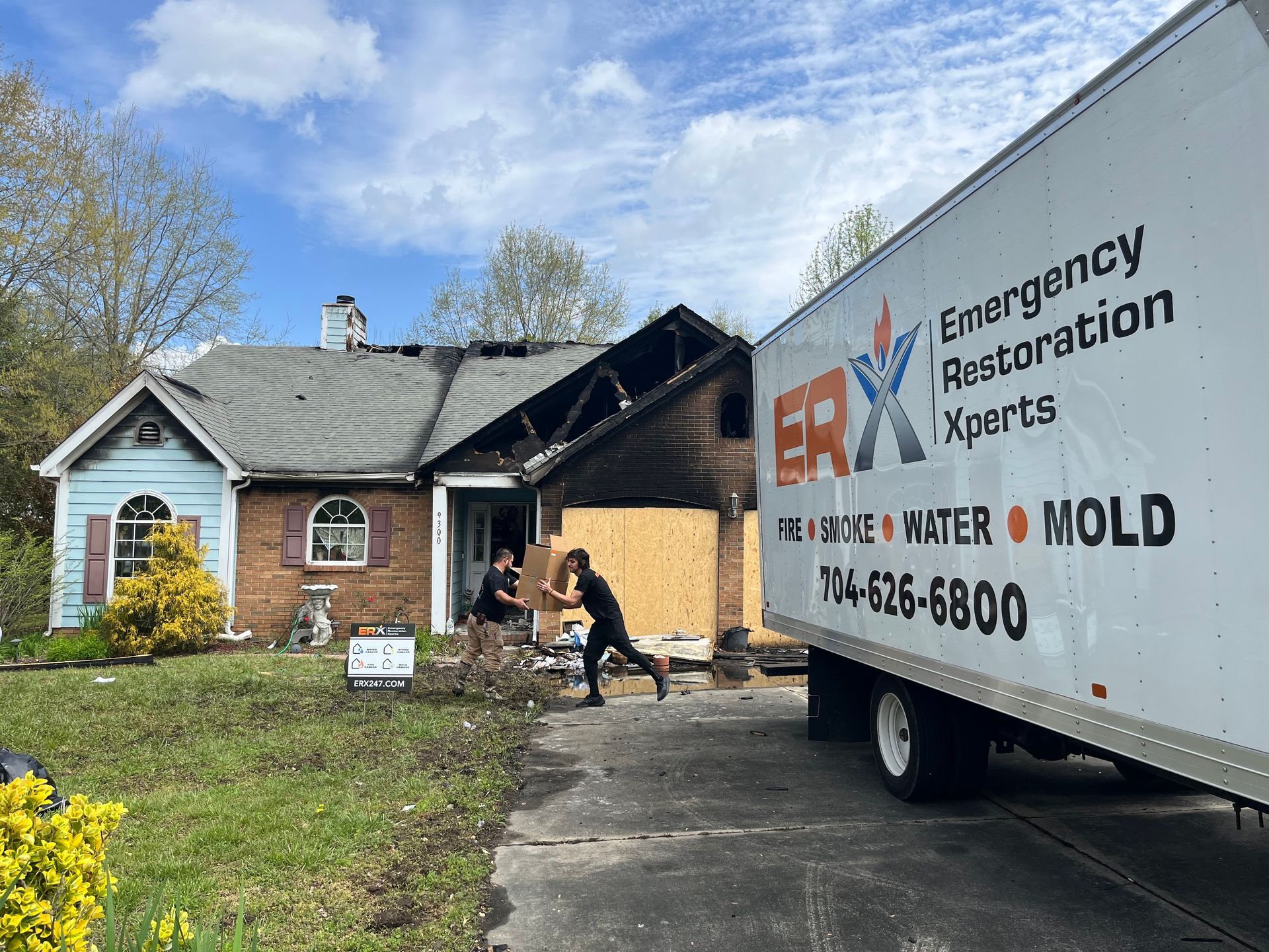 Emergency restoration truck parked outside a damaged house, with a worker near the garage.