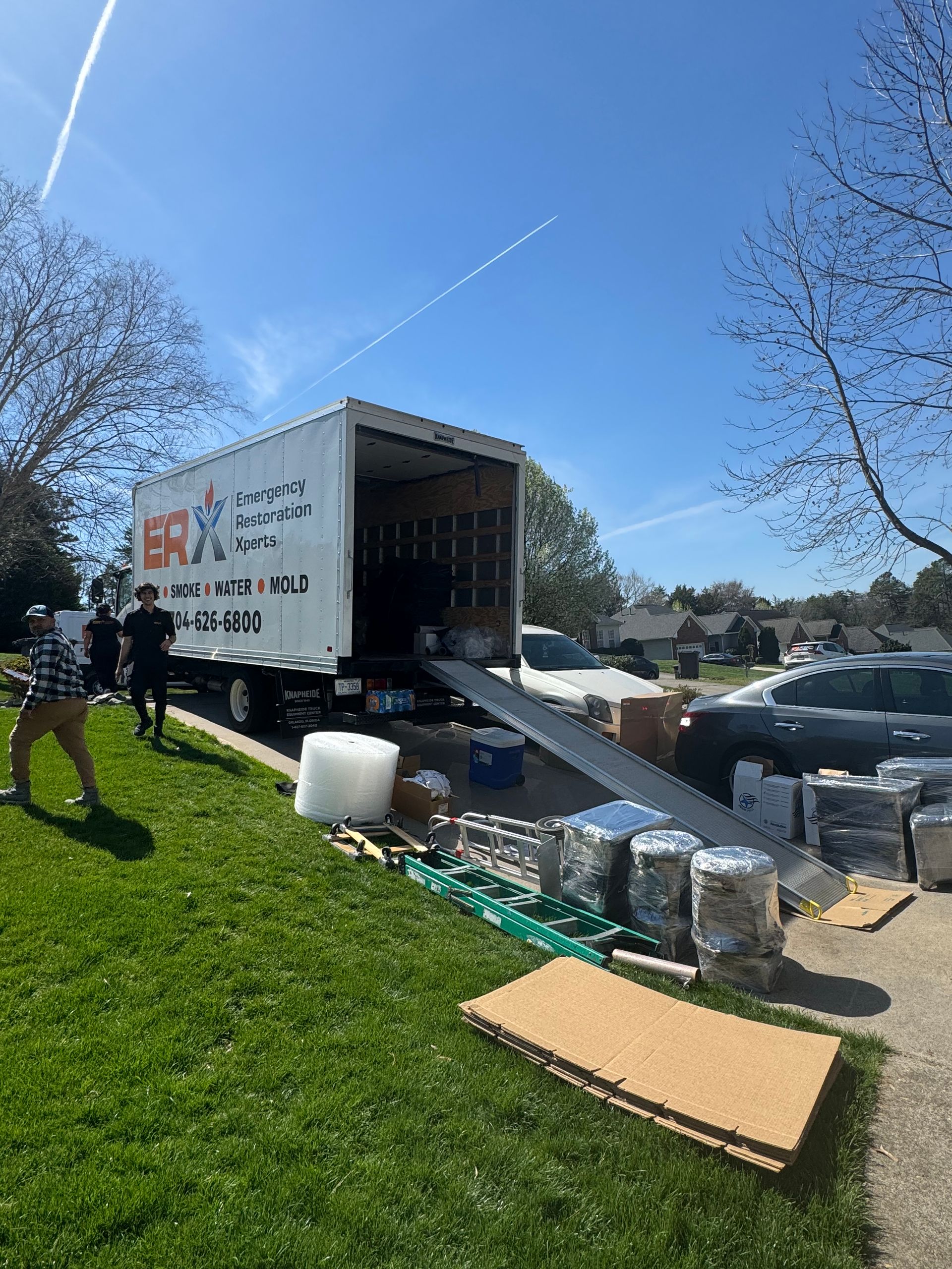 Moving truck unloading white boxes and materials onto a grassy lawn under a blue sky