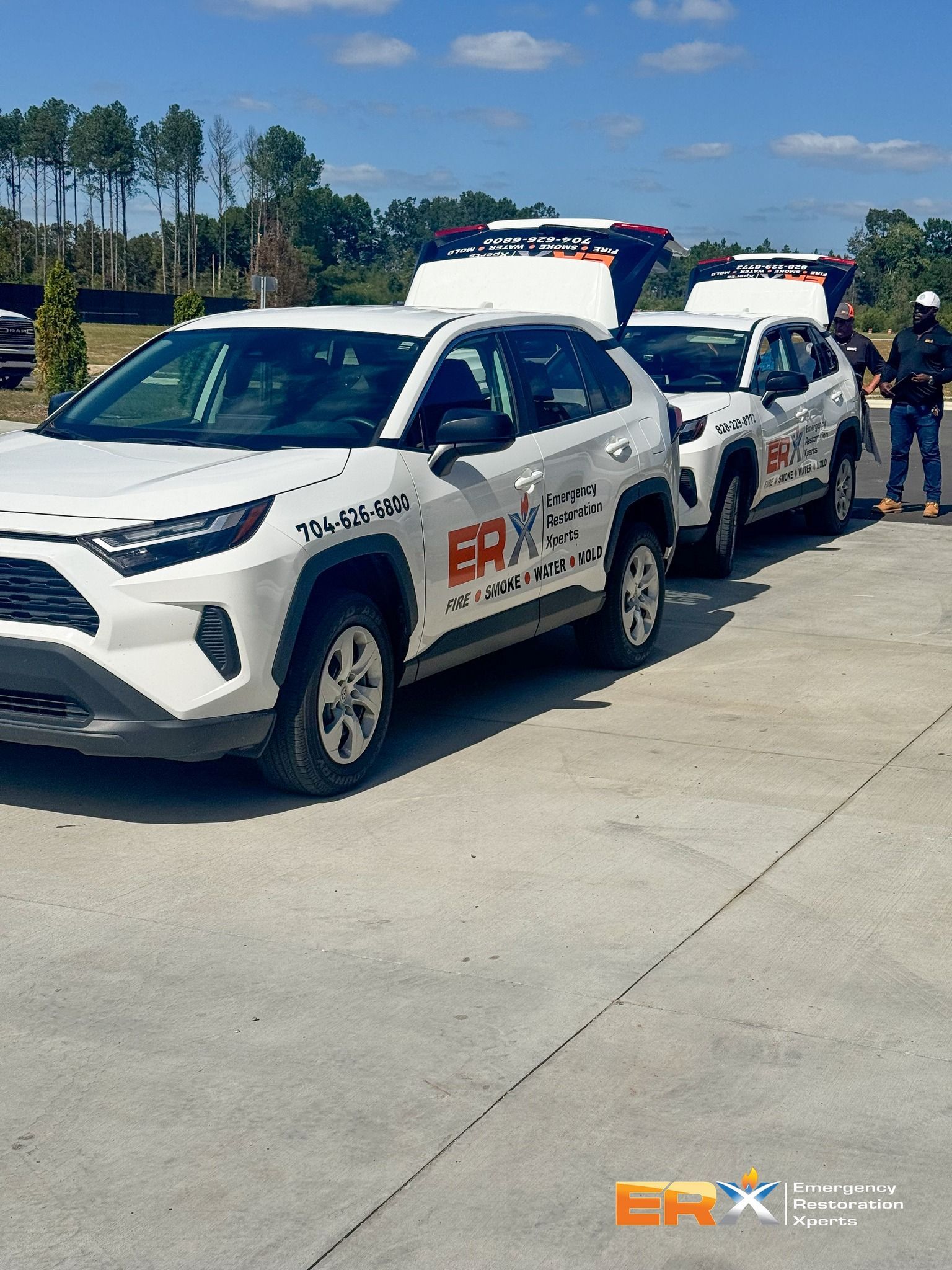 Two white service vehicles with roof lights lined up on a sunny concrete lot.