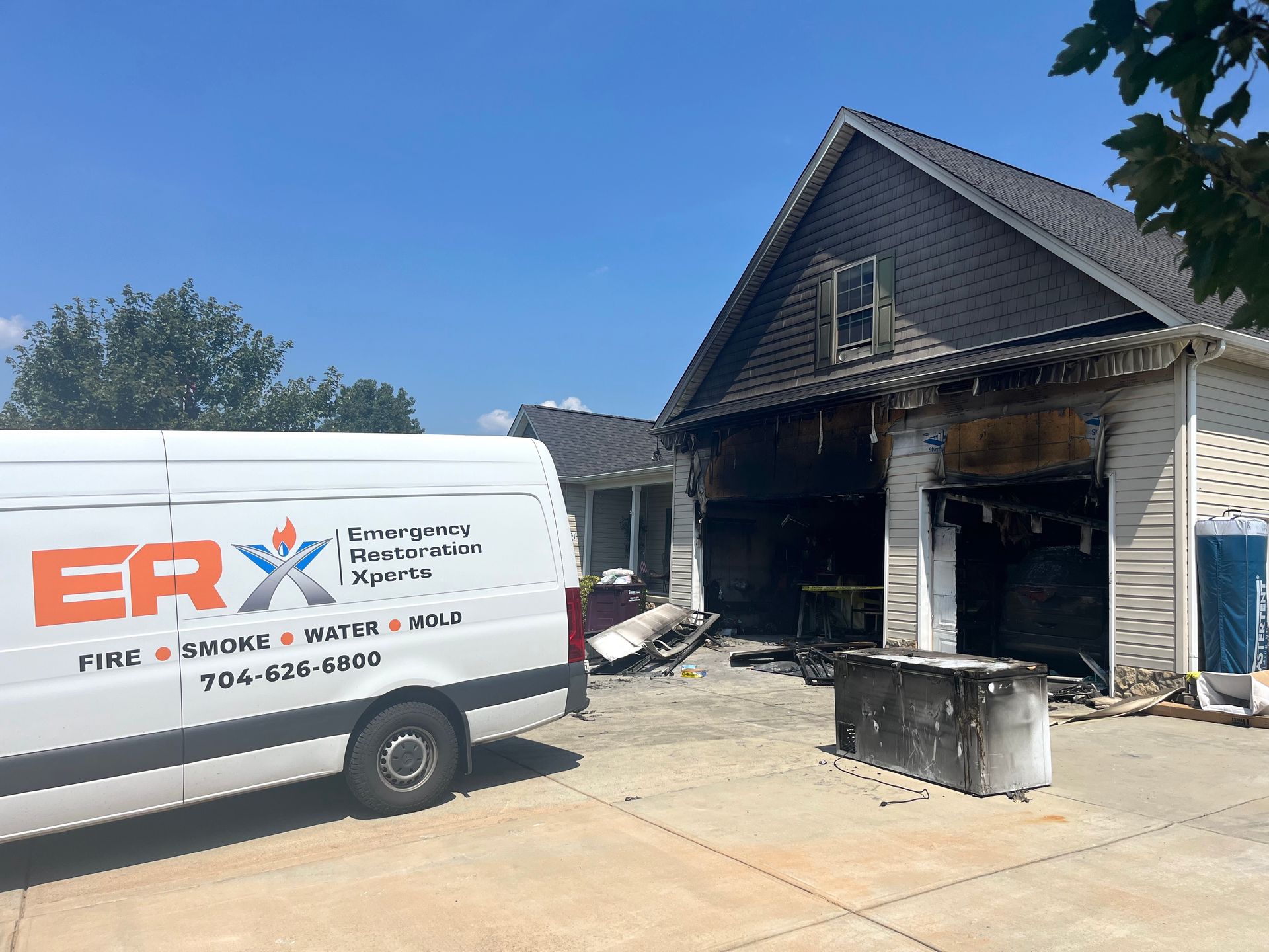 ERX work van outside a fire-damaged house with charred garage and debris in driveway
