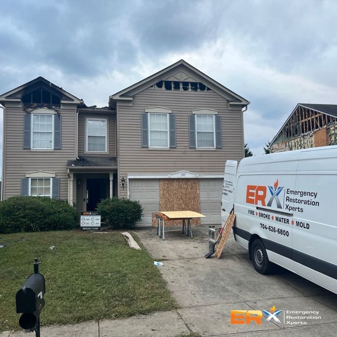 Two-story house with roof damage and an ERX service van parked in the driveway after storm damage
