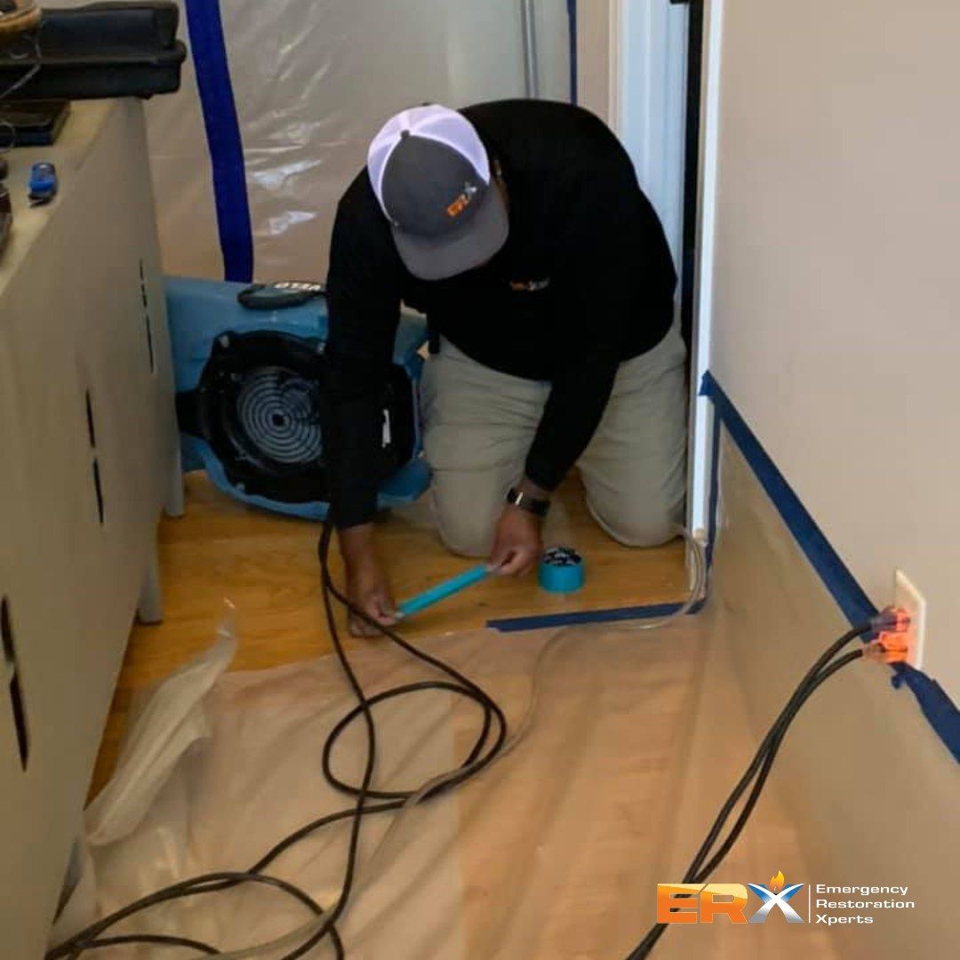Worker kneeling on a floor, checking cables beside a blue fan in a narrow hallway.