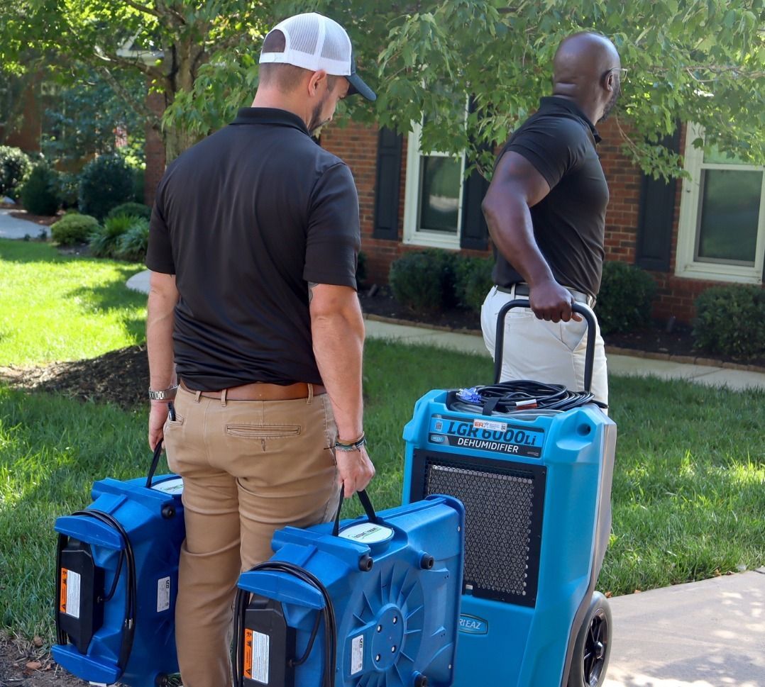 Two men carry blue portable equipment on a sidewalk in a sunny residential area