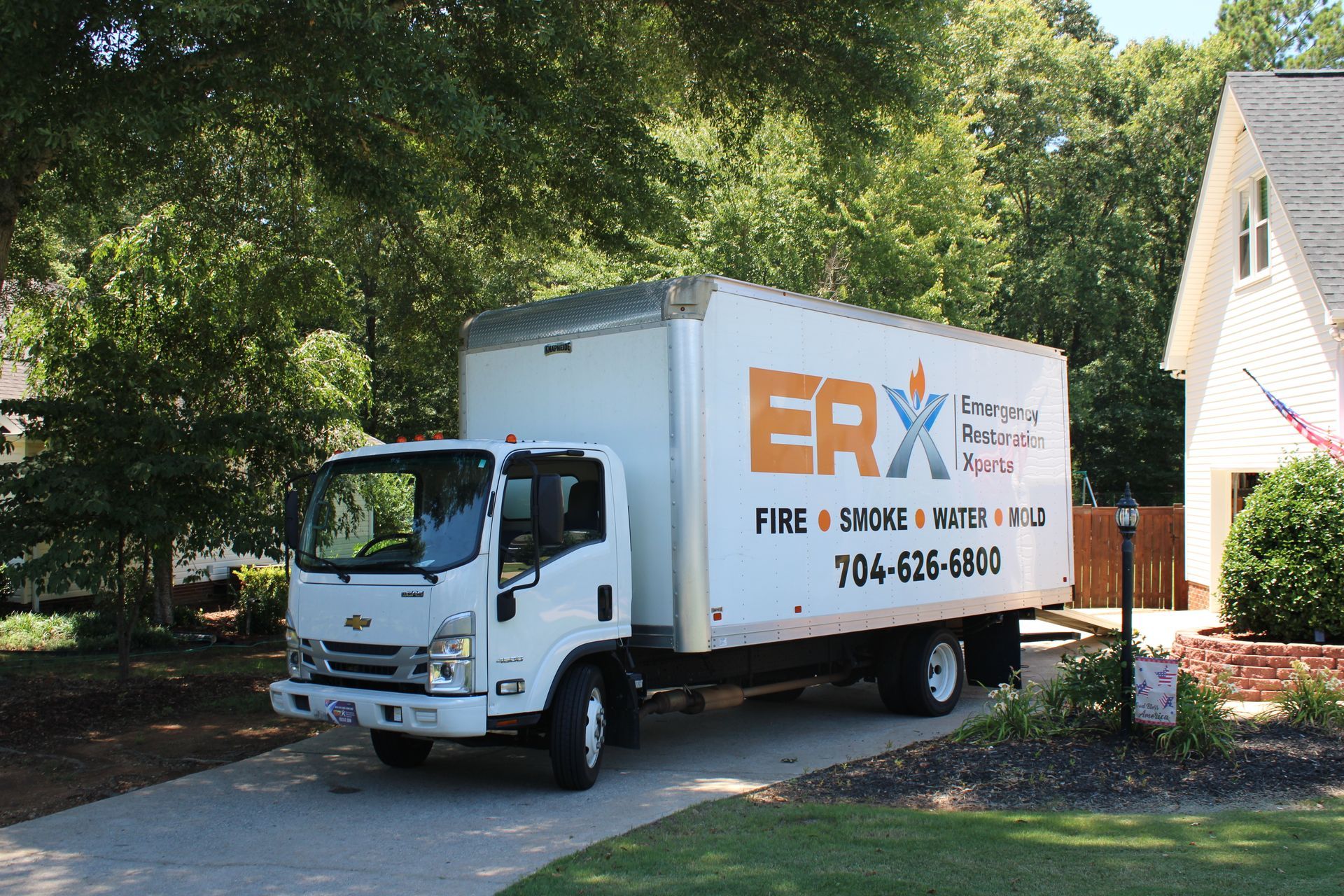 White ERX moving truck parked in a driveway beside a house and trees