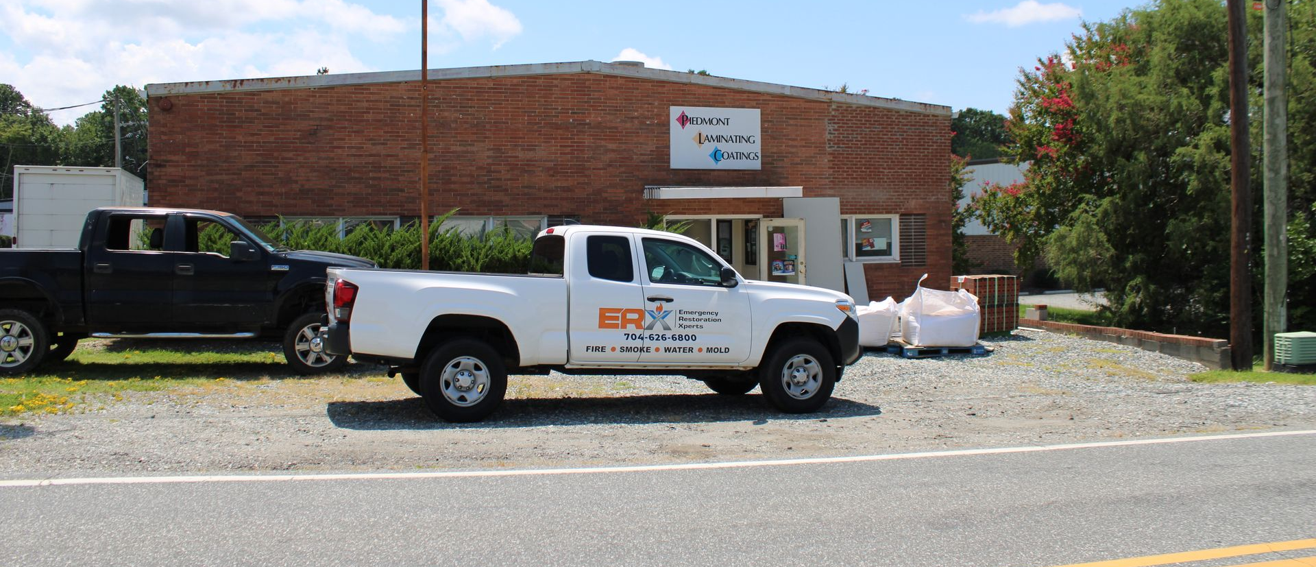 White and black pickup trucks parked outside a brick building with a sign near the entrance